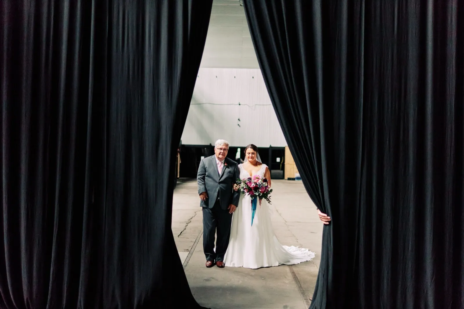 Maggie and her father walk toward the ceremony framed through a narrow opening between two tall black curtains — Tim Larsen Photography, Brainerd Lakes MN