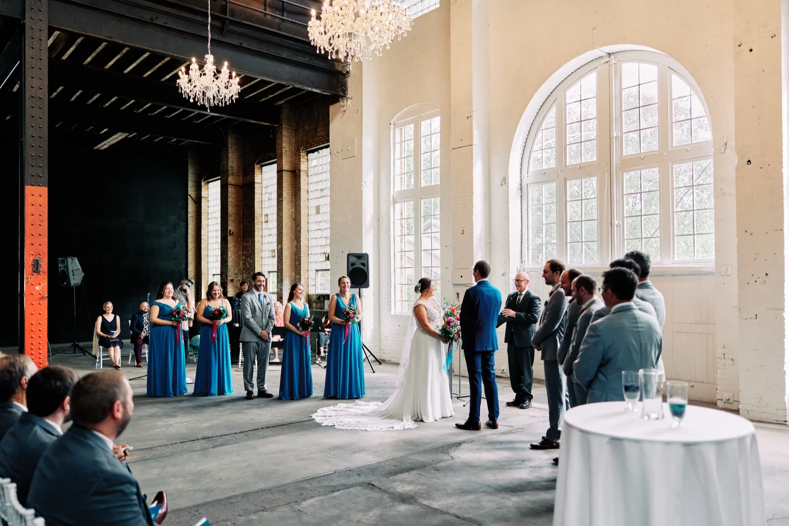 Maggie and Craig face each other at the altar beneath a tall arched window, with their wedding party in blue dresses and gray suits beside them — Tim Larsen Photography, Brainerd Lakes MN