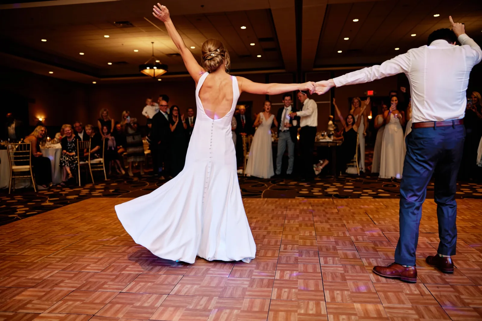 The bride and groom face each other with arms thrown wide on the ballroom dance floor as guests cheer from the edges. — Tim Larsen Photography, Brainerd Lakes MN