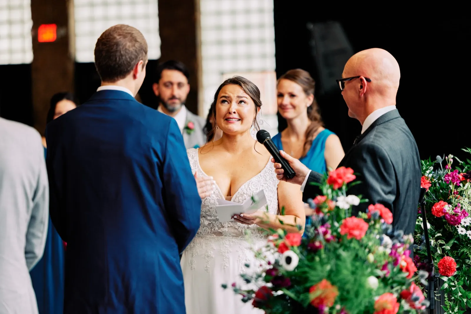 Maggie looks up toward Craig while reading from her vow book as the officiant holds a microphone beside her — Tim Larsen Photography, Brainerd Lakes MN