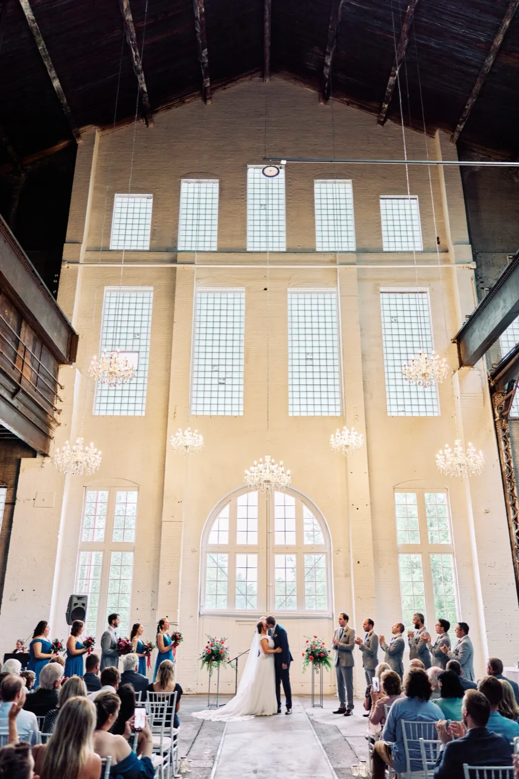 Maggie and Craig share their first kiss at the altar, dwarfed by the soaring brick walls, arched windows, and chandeliers of Northern Pacific Center — Tim Larsen Photography, Brainerd Lakes MN
