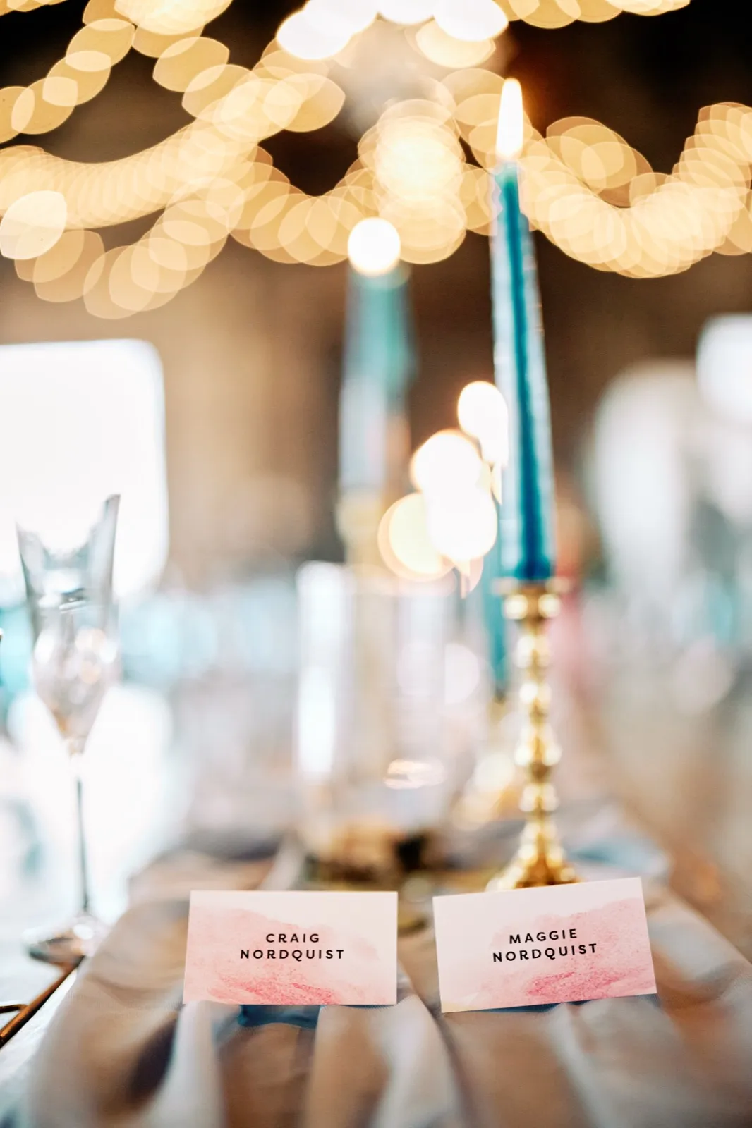 Maggie and Craig's pink watercolor place cards sit beneath blue taper candles and softly glowing reception lights — Tim Larsen Photography, Brainerd Lakes MN