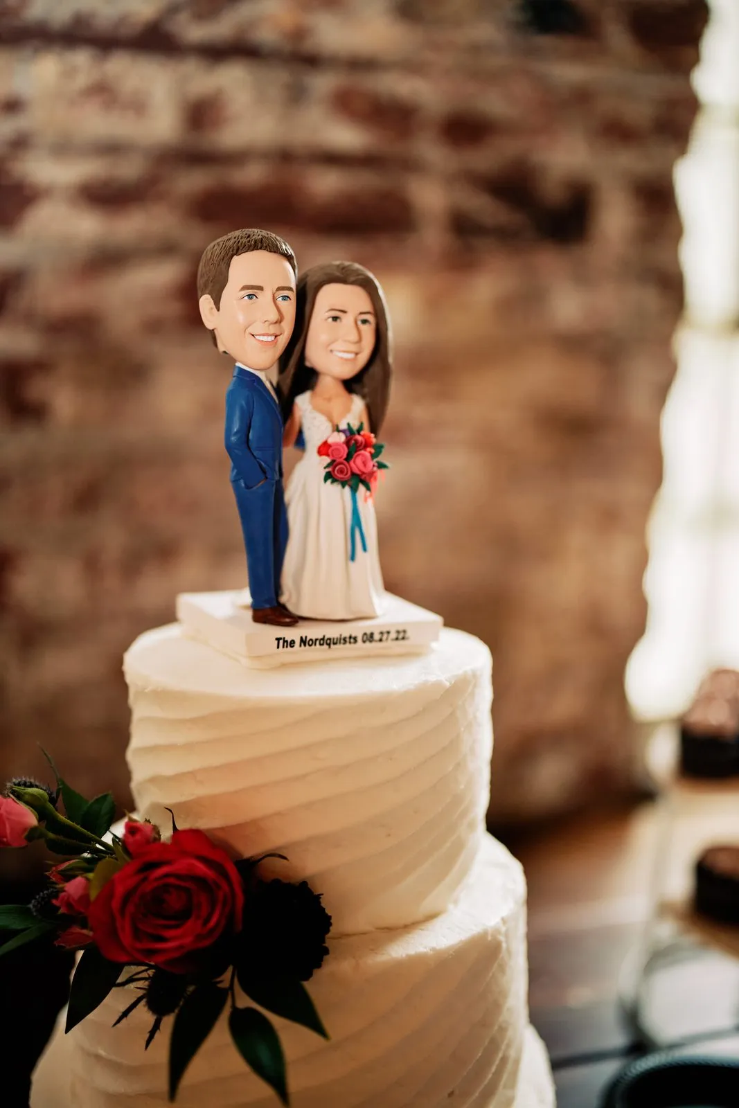 Personalized bobblehead figures of Maggie and Craig top a white buttercream wedding cake decorated with red roses — Tim Larsen Photography, Brainerd Lakes MN