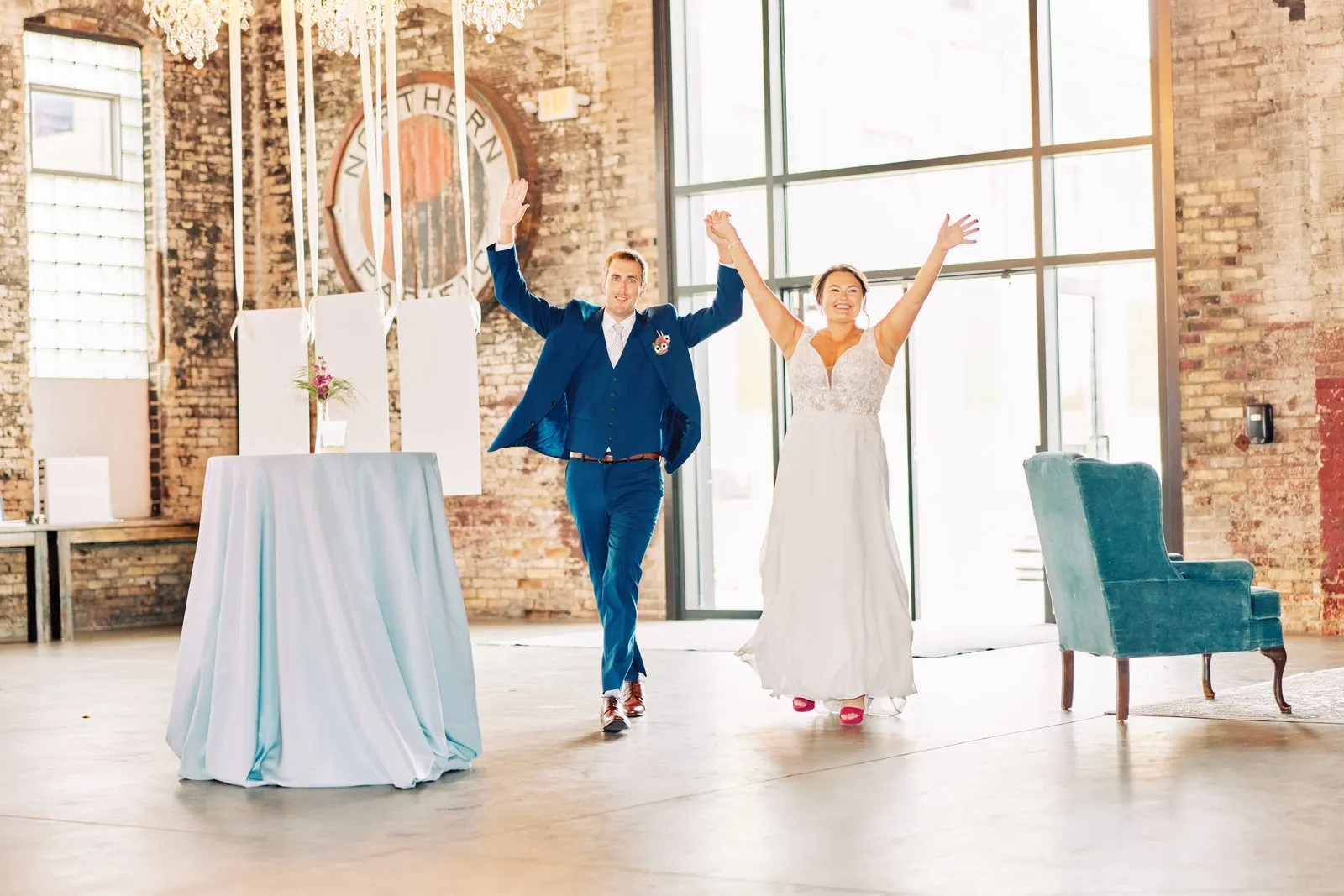 Maggie and Craig enter their reception with both arms raised beside tall windows and the Northern Pacific Center wall sign — Tim Larsen Photography, Brainerd Lakes MN