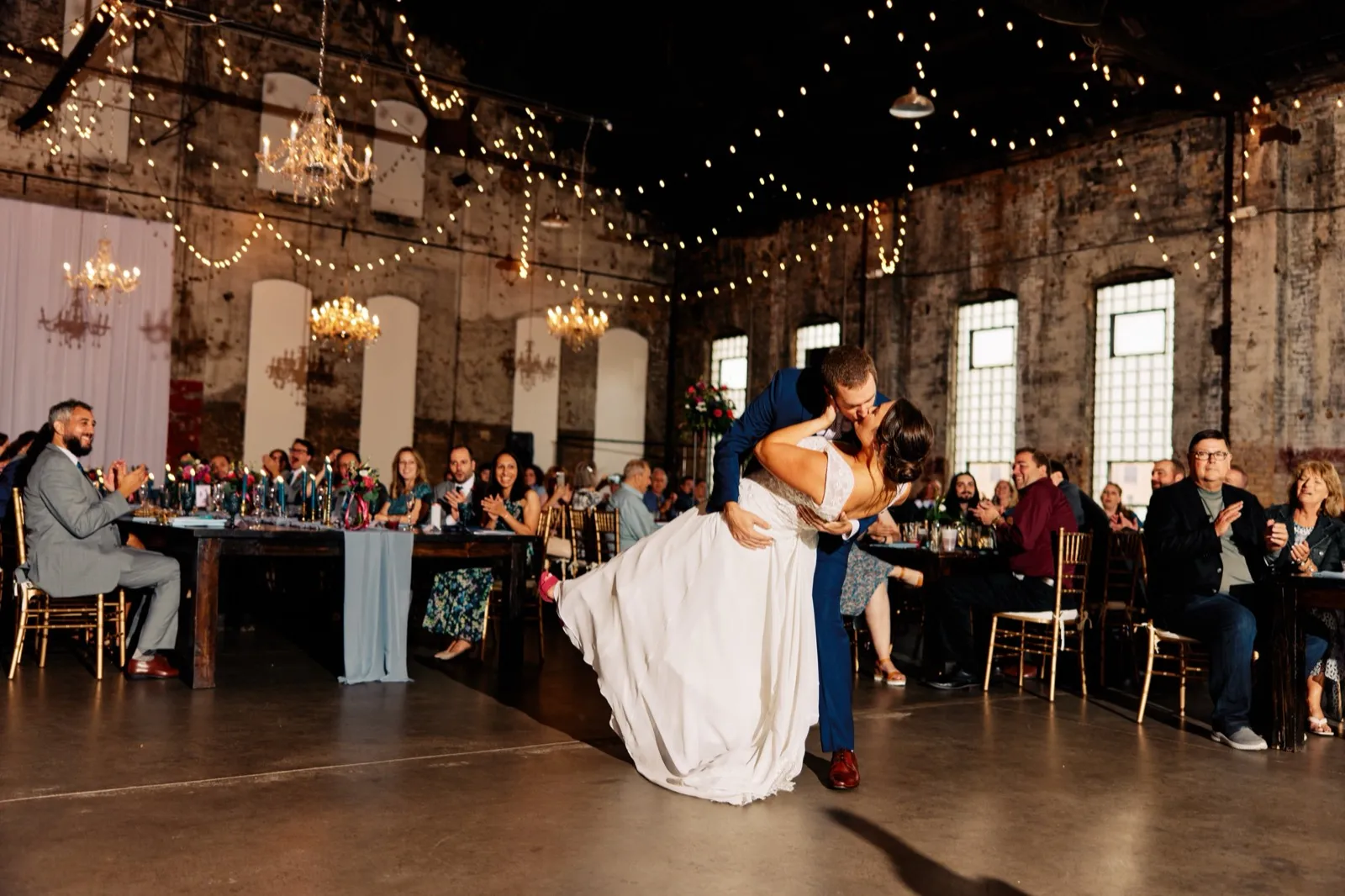 Craig dips Maggie into a kiss on the dance floor as seated guests applaud beneath chandeliers and rows of string lights — Tim Larsen Photography, Brainerd Lakes MN
