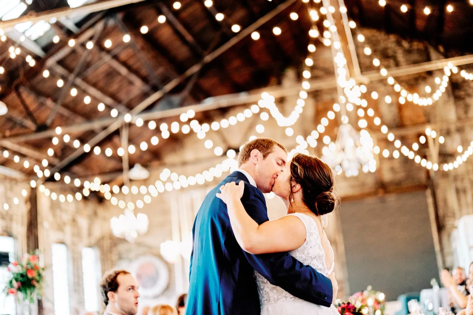 Maggie and Craig kiss on the dance floor beneath an expansive canopy of bistro lights strung across the exposed wooden rafters — Tim Larsen Photography, Brainerd Lakes MN
