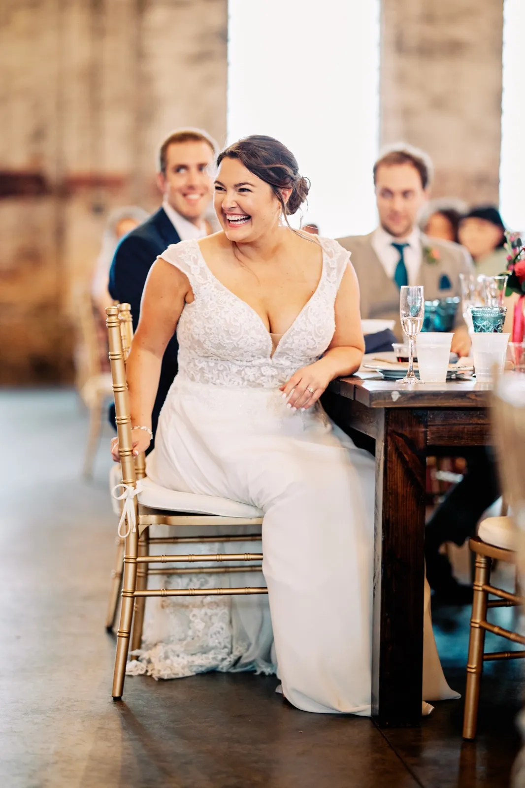 Maggie leans back laughing in a gold chair at the reception table while Craig smiles behind her during the toasts — Tim Larsen Photography, Brainerd Lakes MN