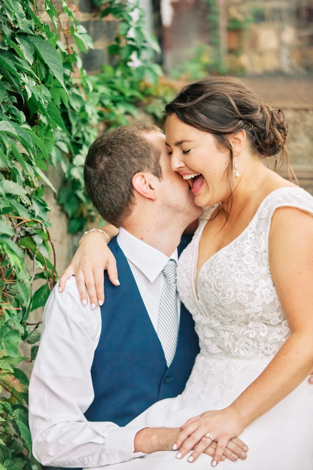 Craig kisses Maggie's cheek as she laughs against an ivy-covered brick wall — Tim Larsen Photography, Brainerd Lakes MN