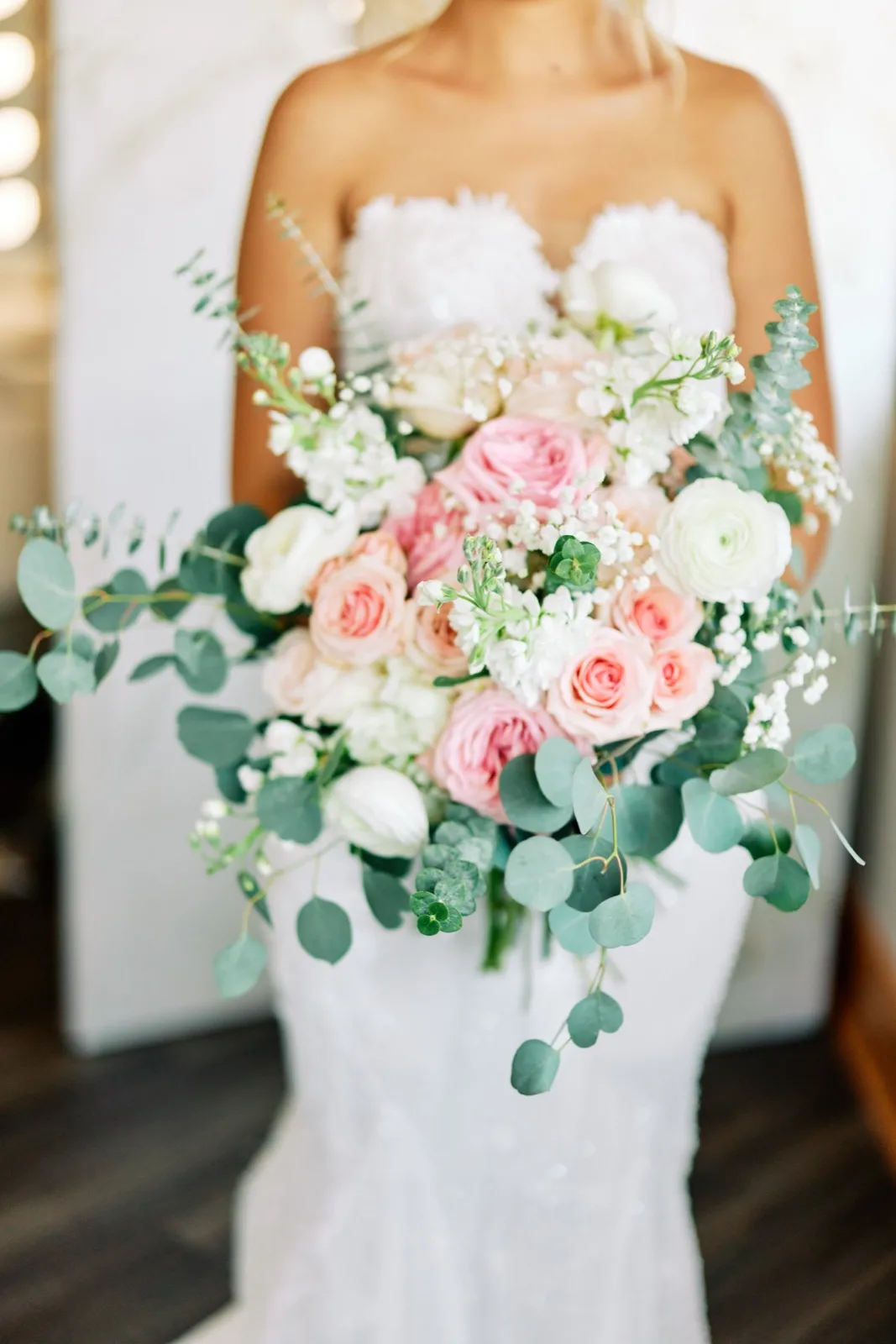 The bride holds a cascading bouquet of pink and white roses, ranunculus, and trailing eucalyptus against her white gown. — Tim Larsen Photography, Twin Cities MN