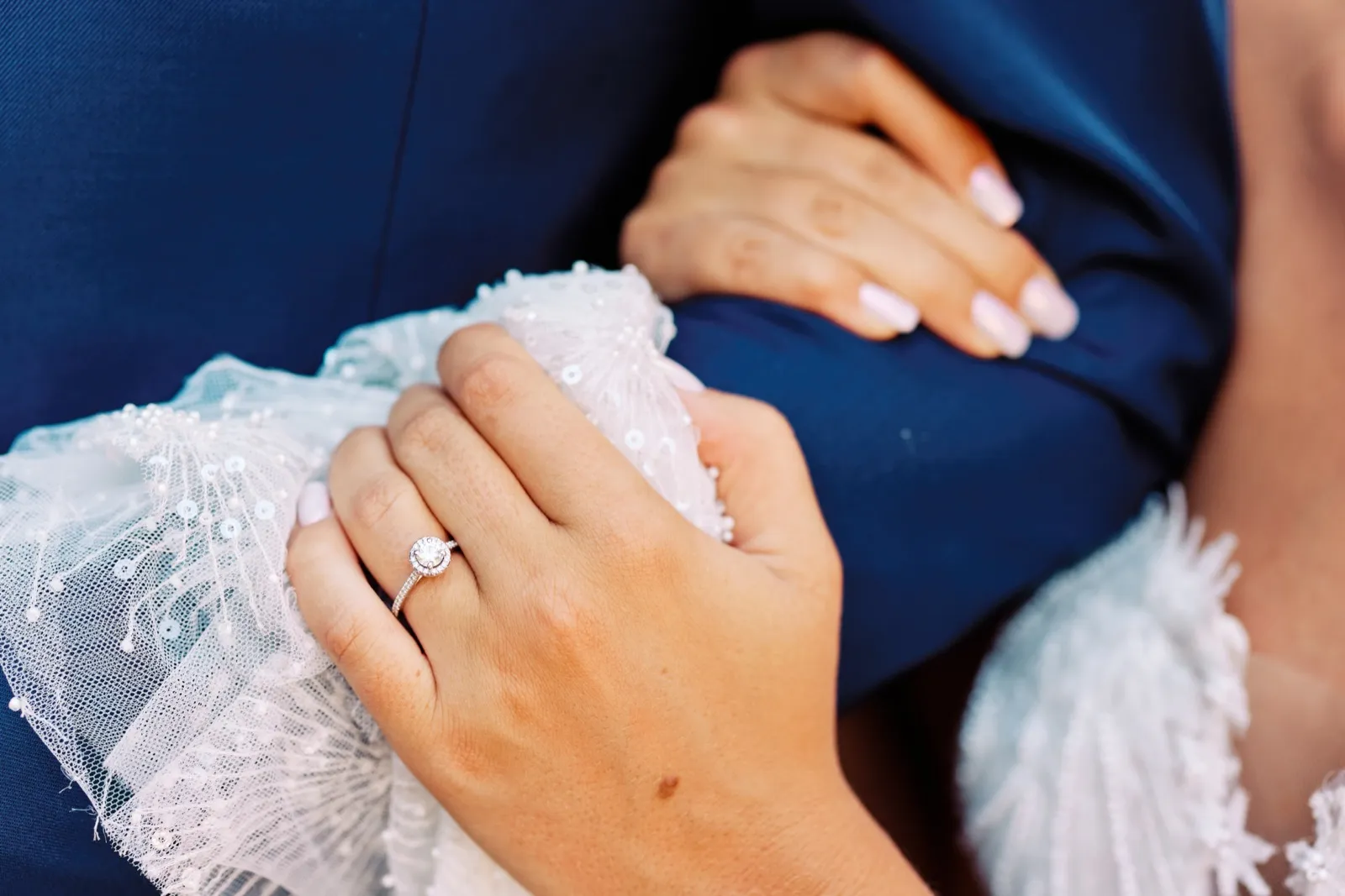 A close-up of the bride's hand resting on the groom's navy suit sleeve, her halo engagement ring visible against the lace of her dress. — Tim Larsen Photography, Twin Cities MN