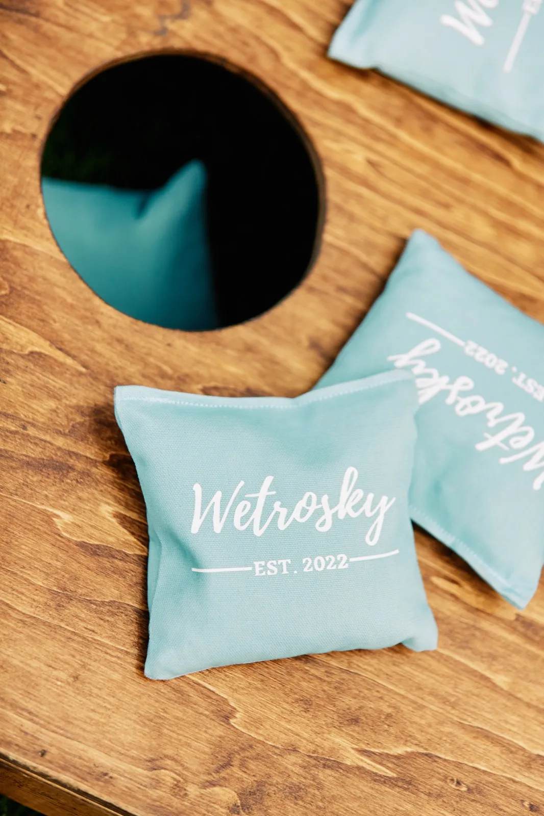 Custom dusty-blue cornhole bags printed with the name Wetrosky and the year 2022 rest on a wooden cornhole board. — Tim Larsen Photography, Brainerd Lakes MN