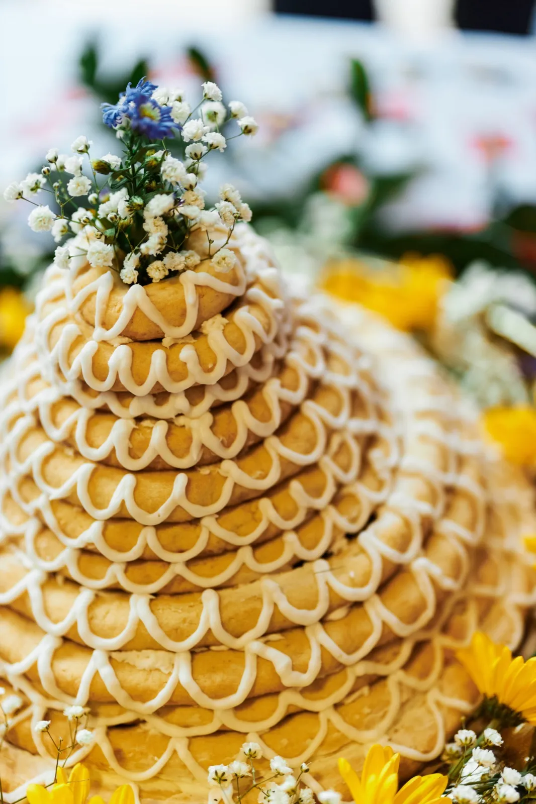 A traditional Norwegian kransekake tower decorated with white icing scallops and topped with baby's breath and blue blossoms sits on a reception table. — Tim Larsen Photography, Minnesota