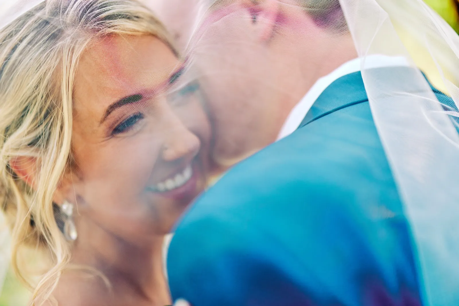 An extreme close-up of the bride smiling as the groom leans into her, both seen through the soft folds of her translucent veil. — Tim Larsen Photography, Twin Cities MN