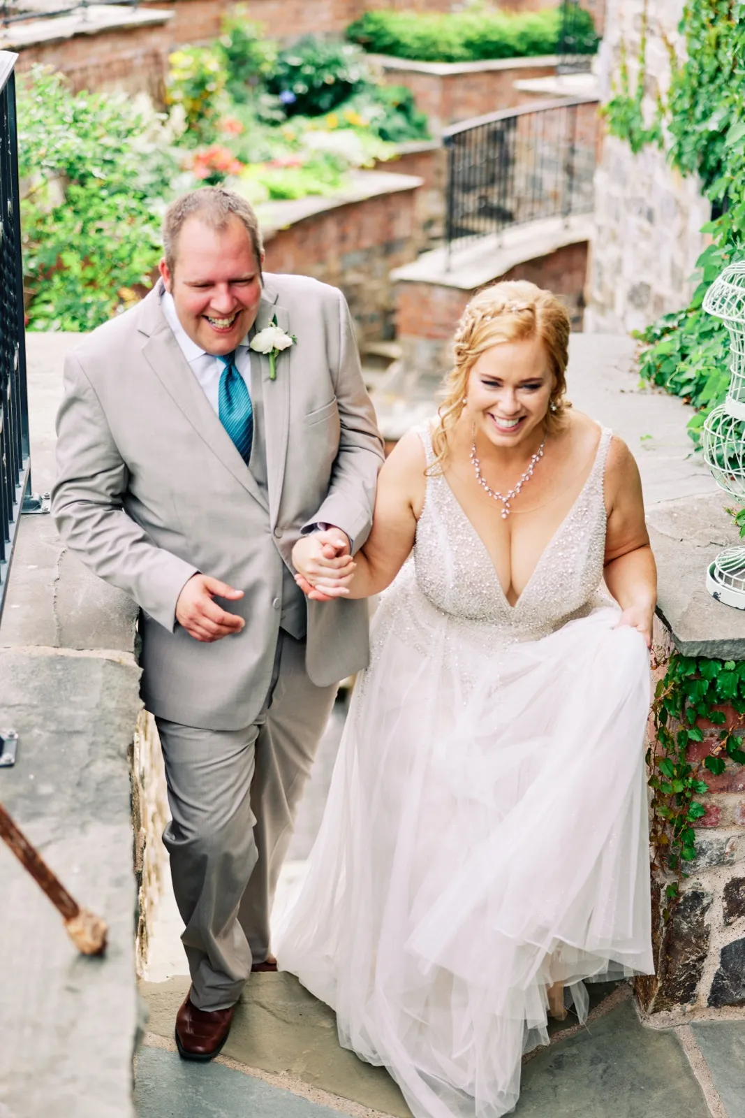 The bride and groom hold hands and laugh as they climb a stone stairway lined with greenery and brick walls. — Tim Larsen Photography, Brainerd Lakes MN