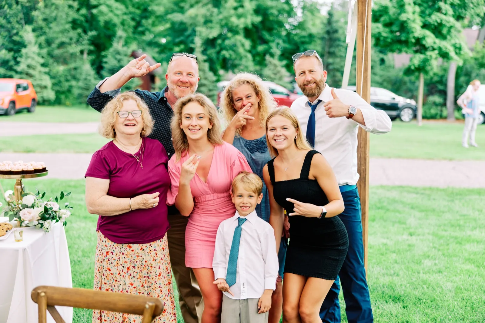 A group of eight family members and guests cluster together on a lawn making playful gestures and silly faces for the camera at an outdoor wedding reception. — Tim Larsen Photography, Brainerd Lakes MN