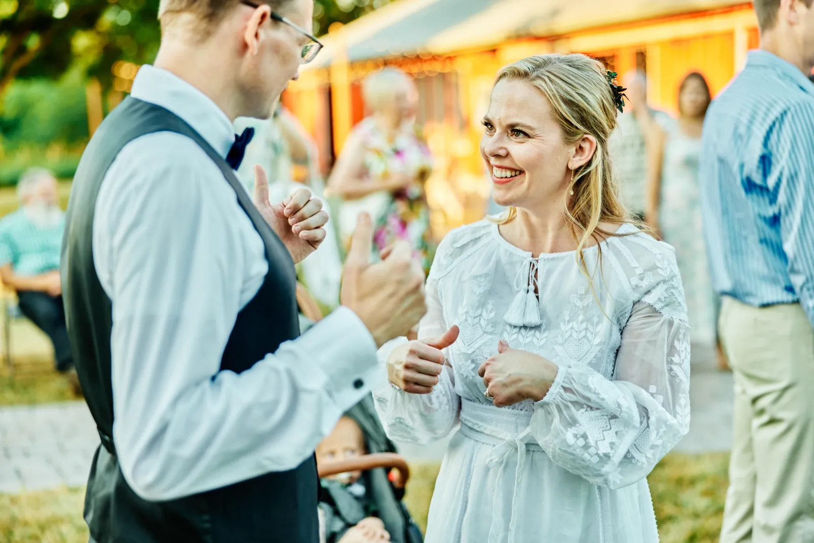 The bride laughs with the groom during cocktail hour outdoors, warm tent light glowing behind them in the background. — Tim Larsen Photography, Minnesota