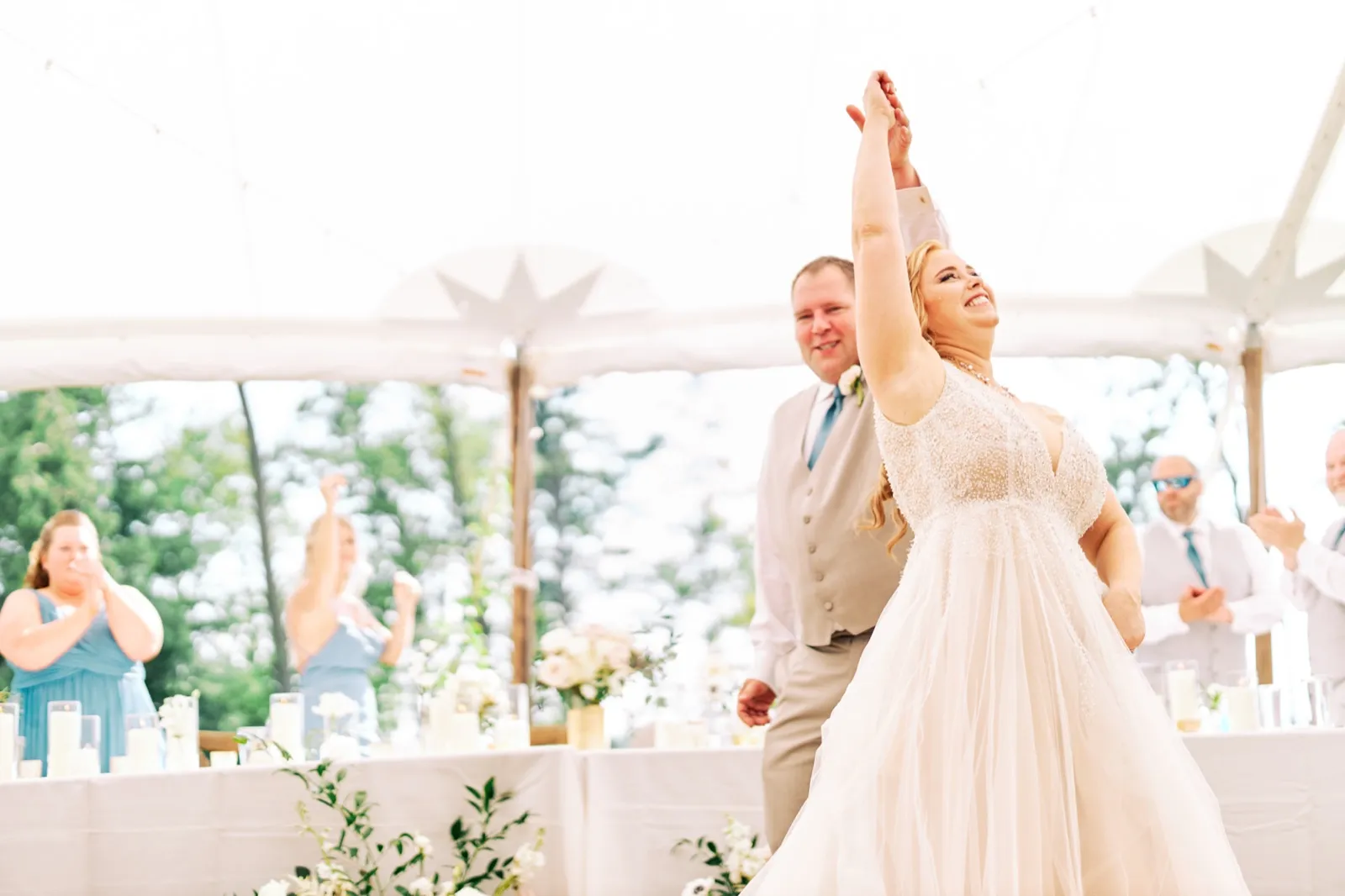 The bride laughs with her arm raised mid-twirl as the groom guides her through their first dance under a reception tent, with guests clapping in the background. — Tim Larsen Photography, Brainerd Lakes MN