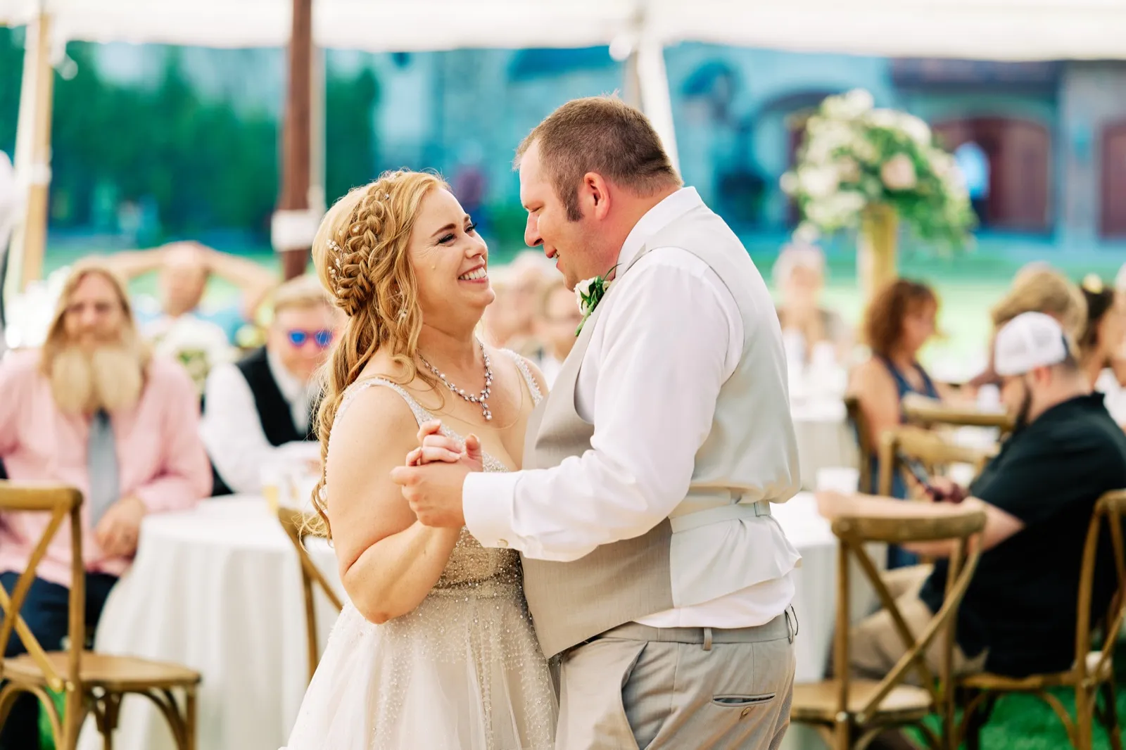 The bride beams up at the groom as they dance close together under a reception tent, with seated guests softly out of focus behind them. — Tim Larsen Photography, Brainerd Lakes MN