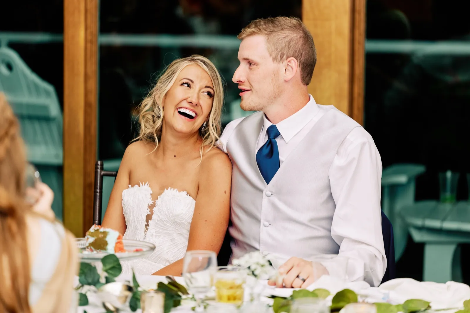 The bride laughs with her head tilted up while the groom turns to look at her during reception toasts at the head table. — Tim Larsen Photography, Twin Cities MN