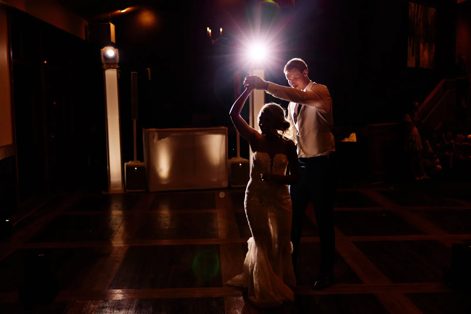 The groom twirls the bride on a dance floor as a single stage light flares behind them, casting them in silhouette. — Tim Larsen Photography, Twin Cities MN