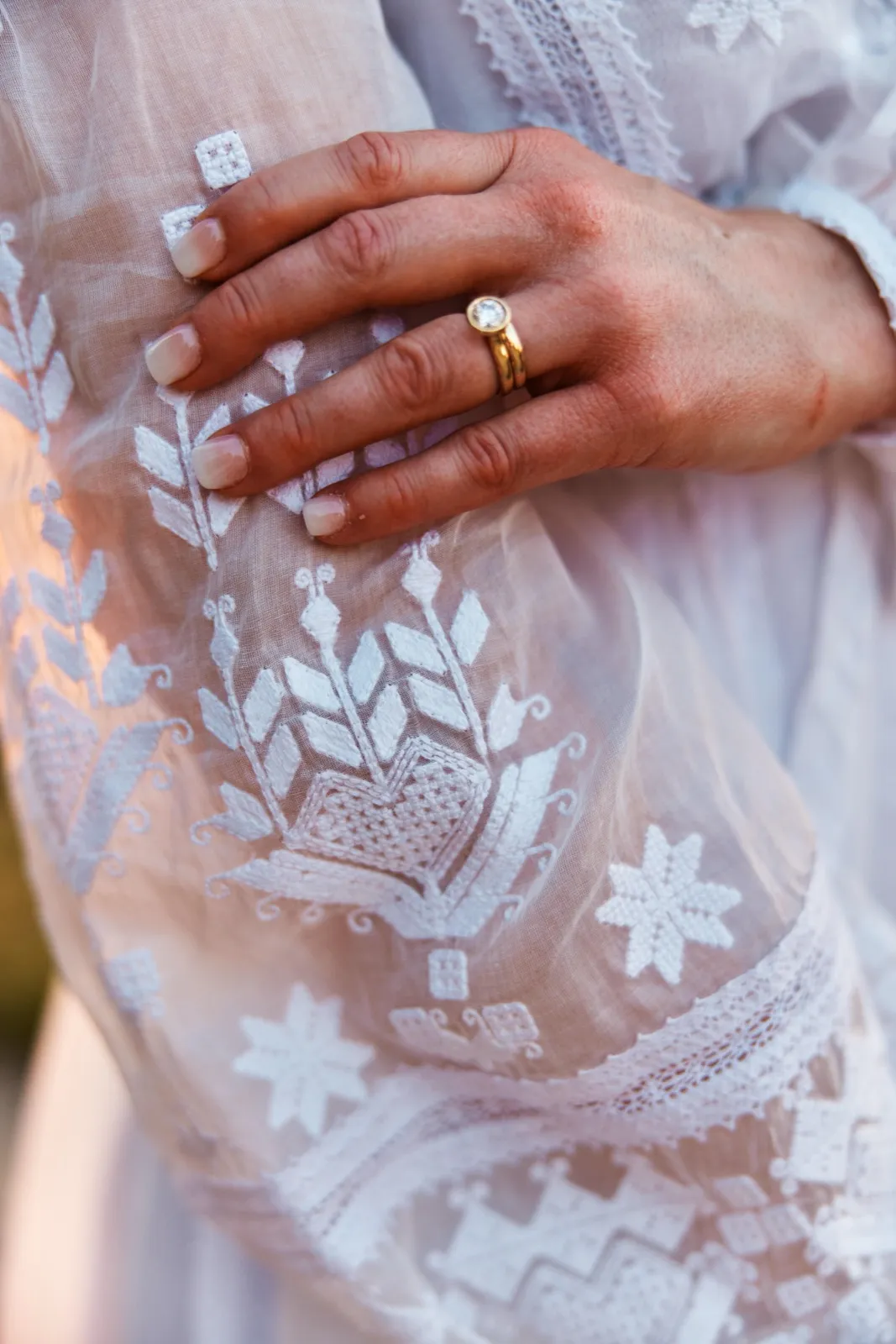 Close-up of the bride's hand with a gold solitaire ring resting against the embroidered white lace of her dress. — Tim Larsen Photography, Minnesota