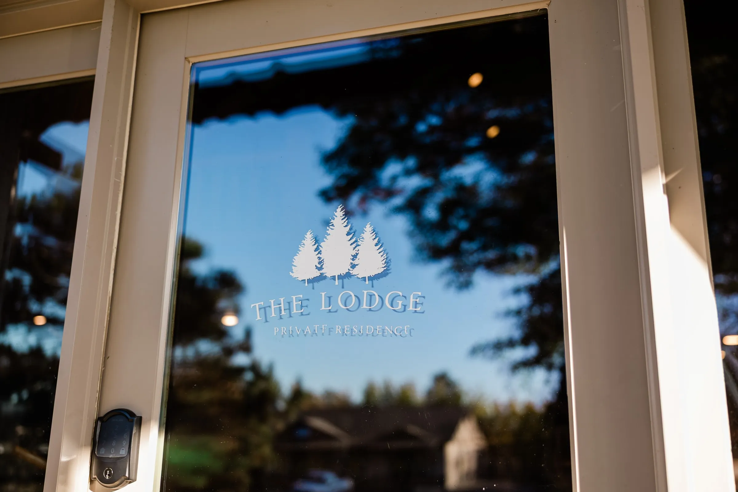 A glass entrance door marked The Lodge Private Residence reflects trees and blue sky — Tim Larsen Photography, Brainerd Lakes MN