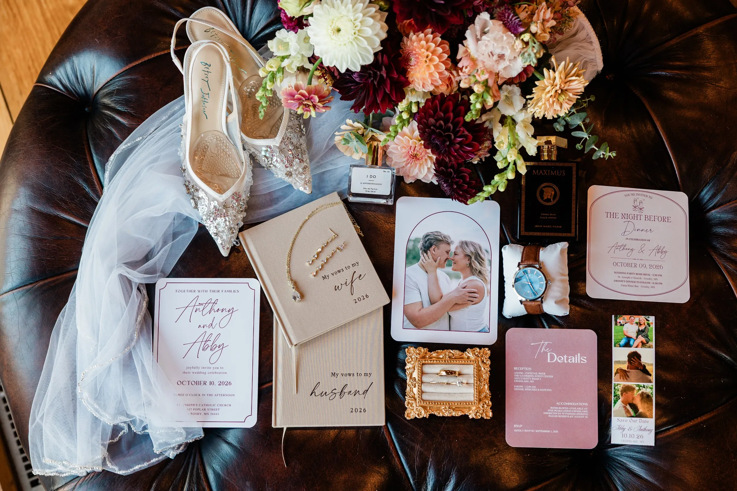 Wedding stationery, vow books, rings, shoes, perfume and a bouquet are arranged on a leather ottoman — Tim Larsen Photography, Brainerd Lakes MN