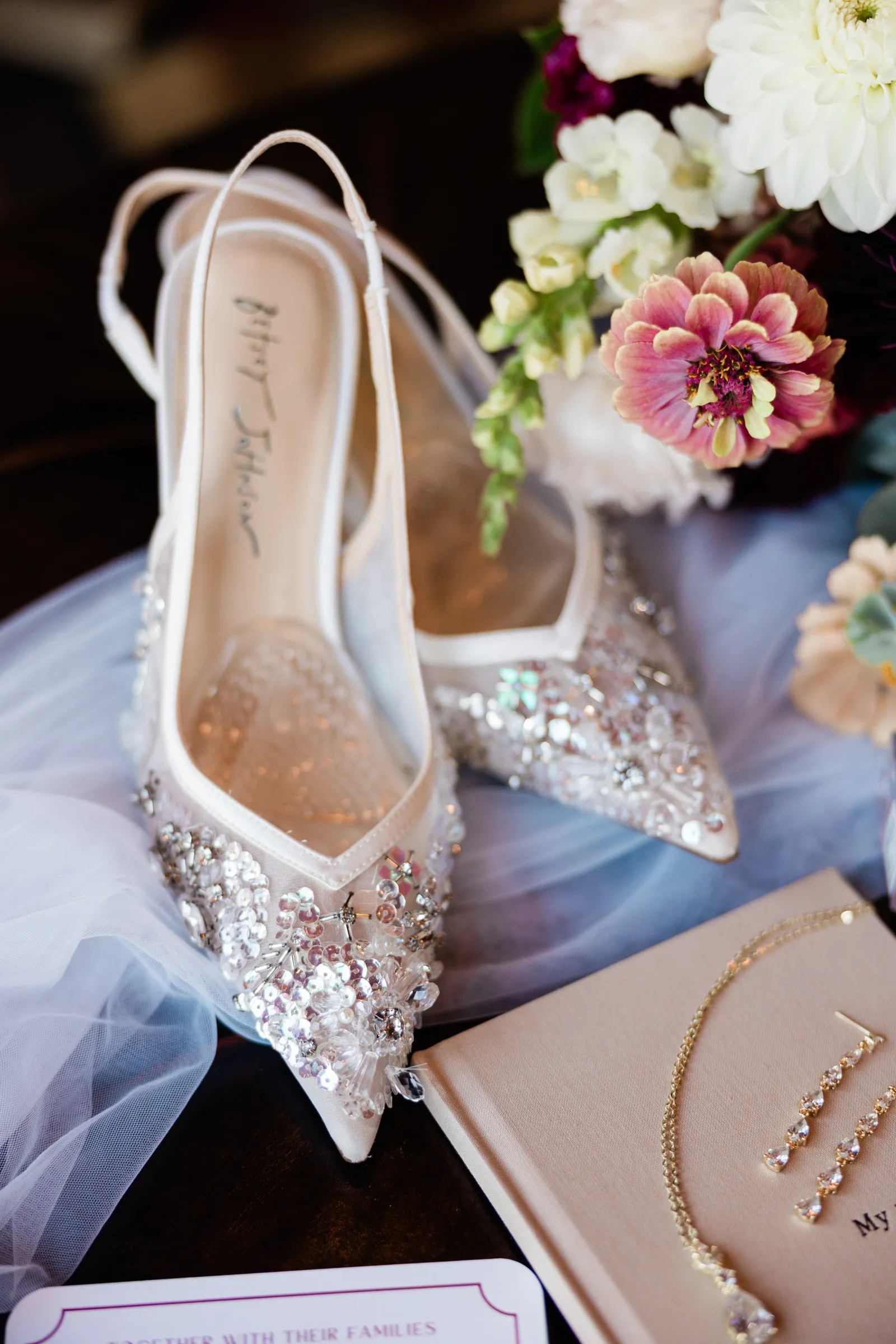 Jeweled bridal shoes rest beside flowers, a veil and gold jewelry on a leather surface at The Gathering Lodge — Tim Larsen Photography, Brainerd Lakes MN