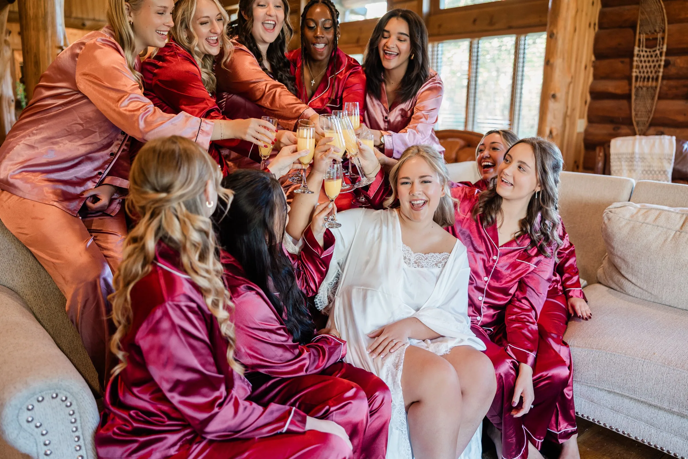 The bride and attendants raise their glasses together while gathered around a lodge sofa at The Gathering Lodge — Tim Larsen Photography, Brainerd Lakes MN