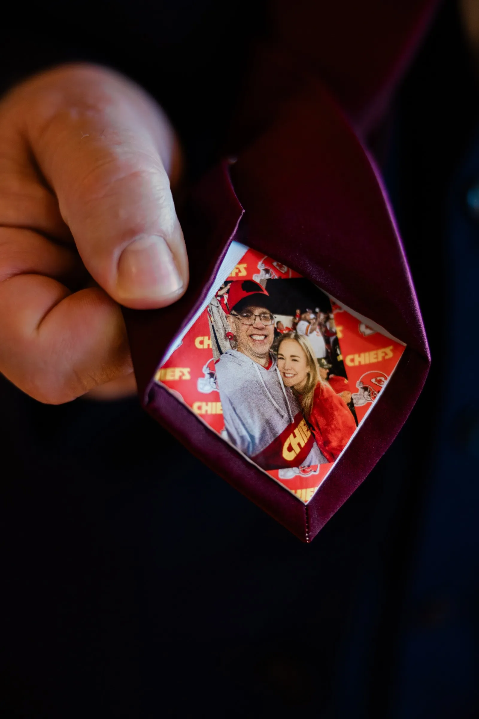 A hand opens a burgundy tie to reveal a printed photograph of two people against a Chiefs backdrop — Tim Larsen Photography, Brainerd Lakes MN