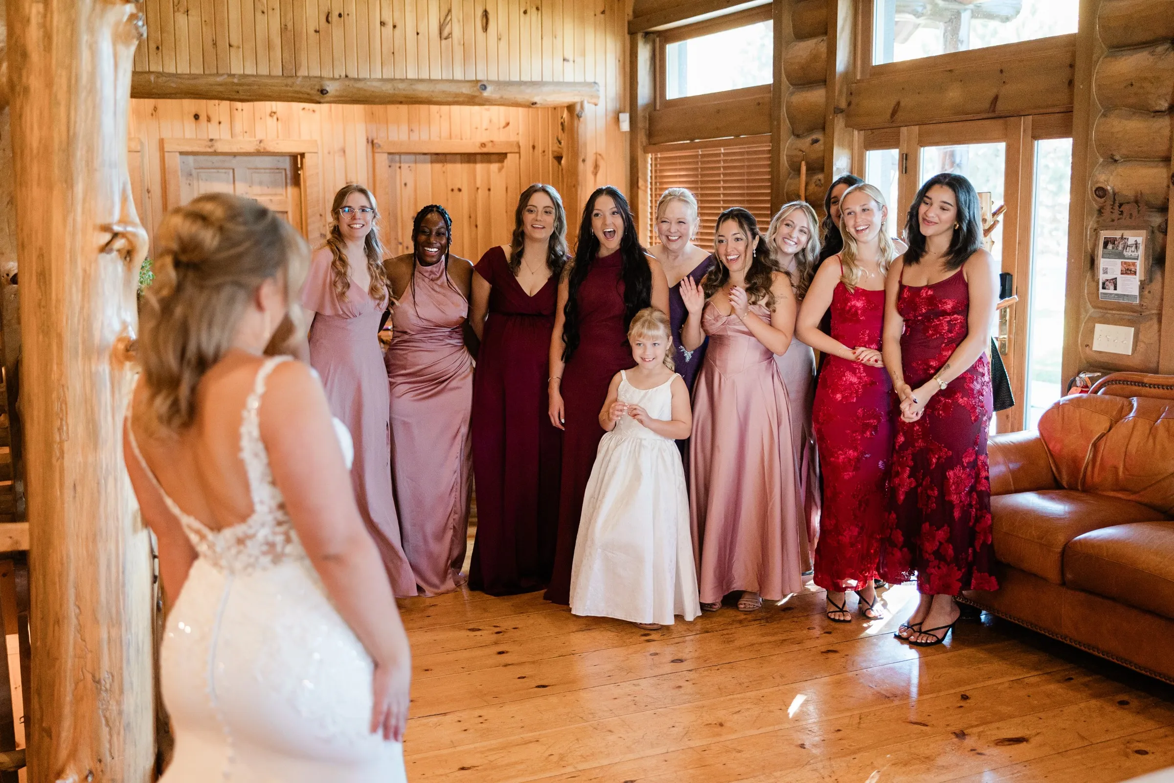 The bride faces a group of smiling women and a young girl as they react to seeing her gown — Tim Larsen Photography, Brainerd Lakes MN
