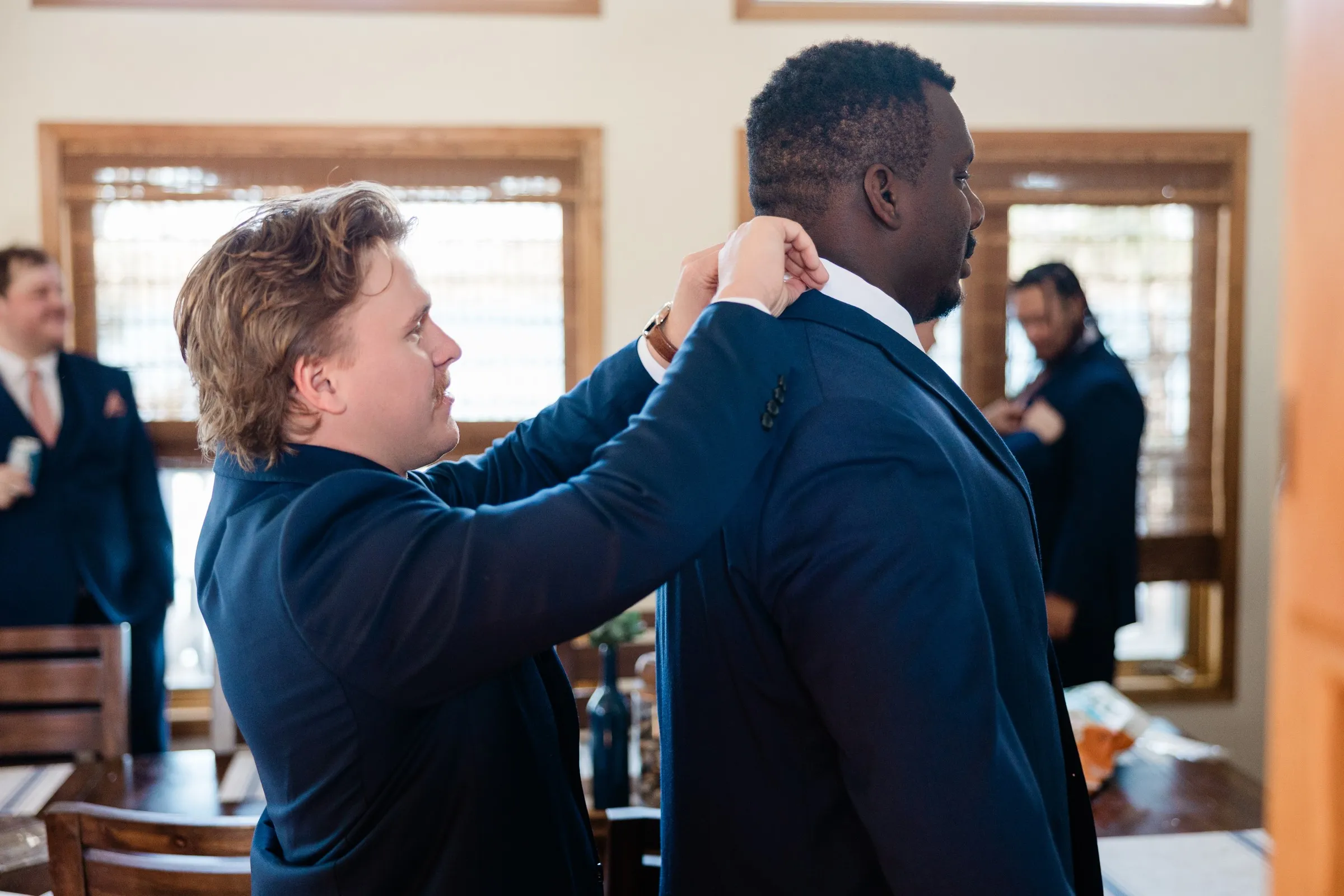 The groom reaches up to straighten a groomsman’s collar while two other men stand in the room — Tim Larsen Photography, Brainerd Lakes MN