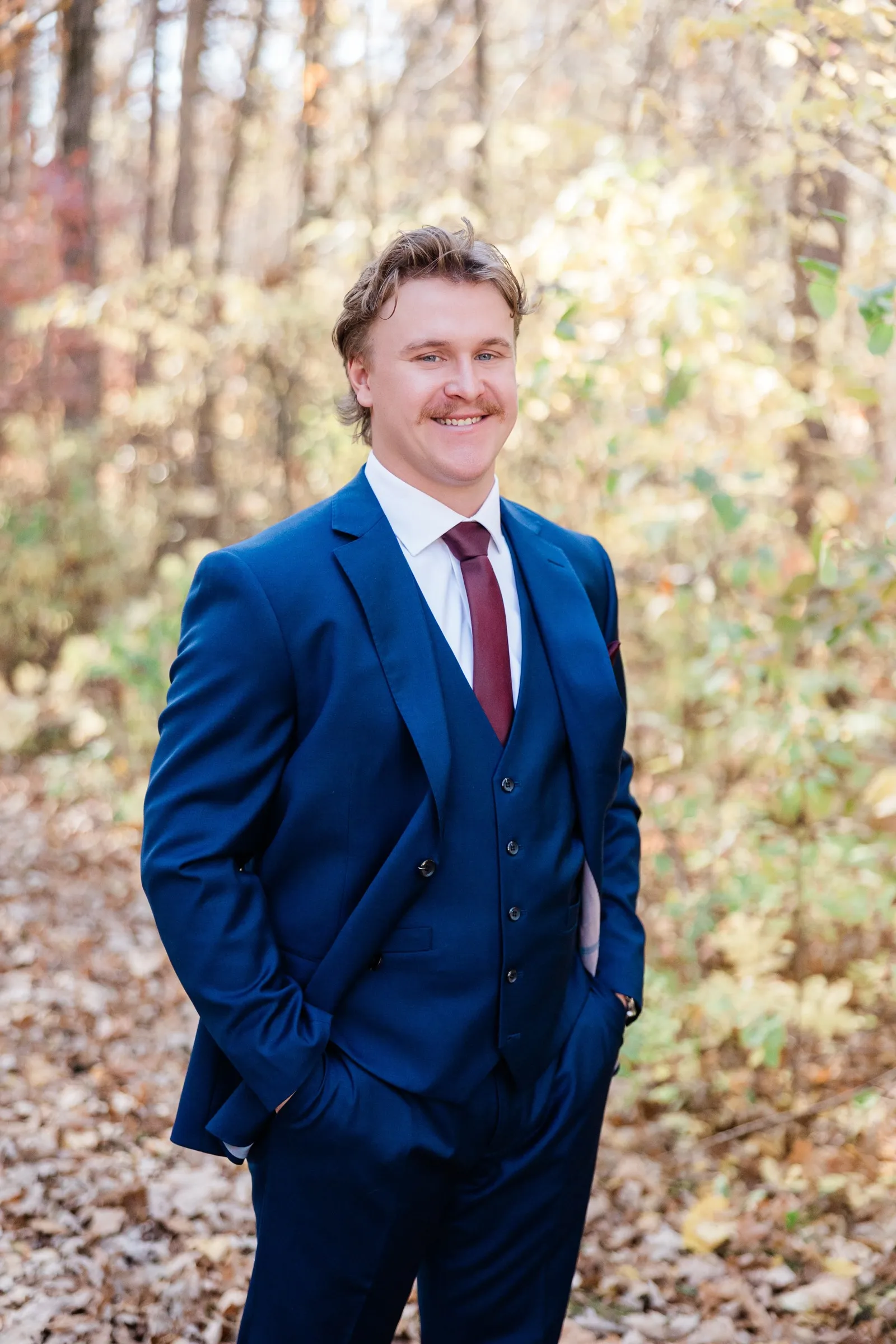 The groom smiles with his hands in his pockets on a leaf-covered woodland path — Tim Larsen Photography, Brainerd Lakes MN