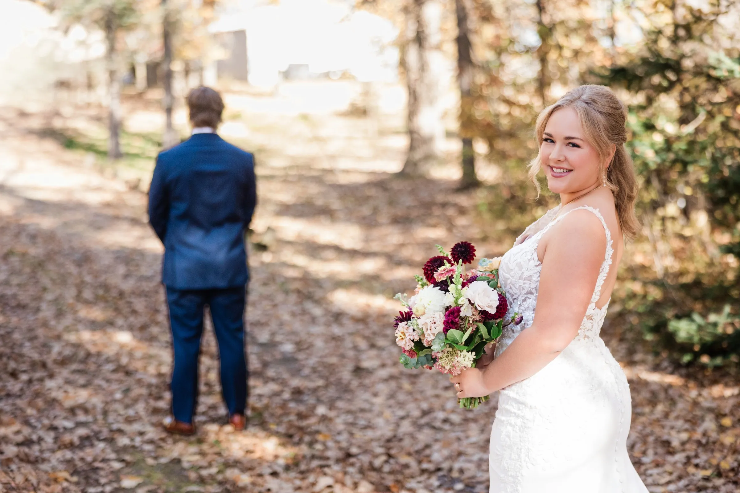 The bride holds a burgundy and blush bouquet while the groom stands facing away farther down the path — Tim Larsen Photography, Brainerd Lakes MN