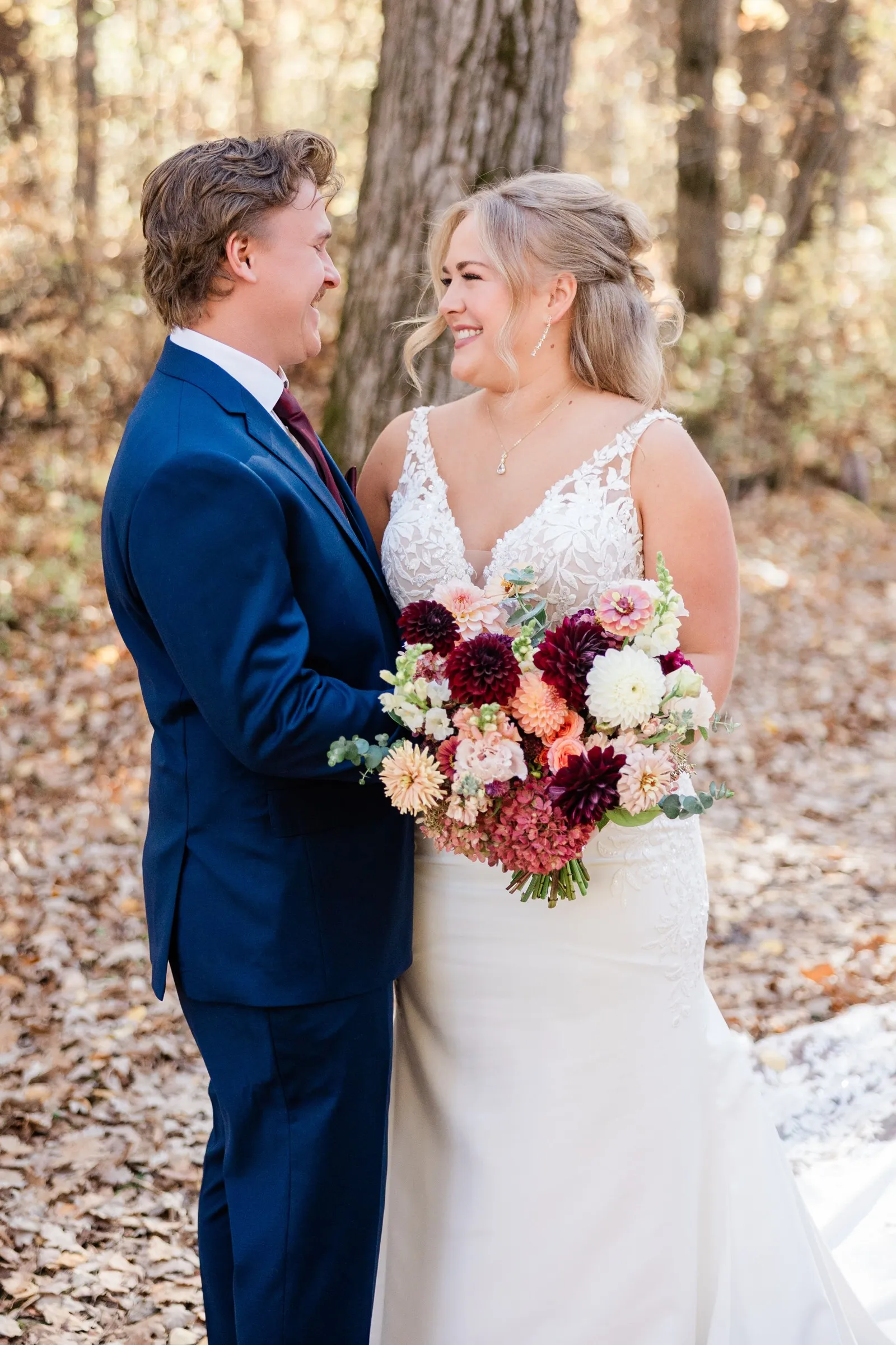 The bride and groom smile at each other with a large burgundy and peach bouquet between them — Tim Larsen Photography, Brainerd Lakes MN