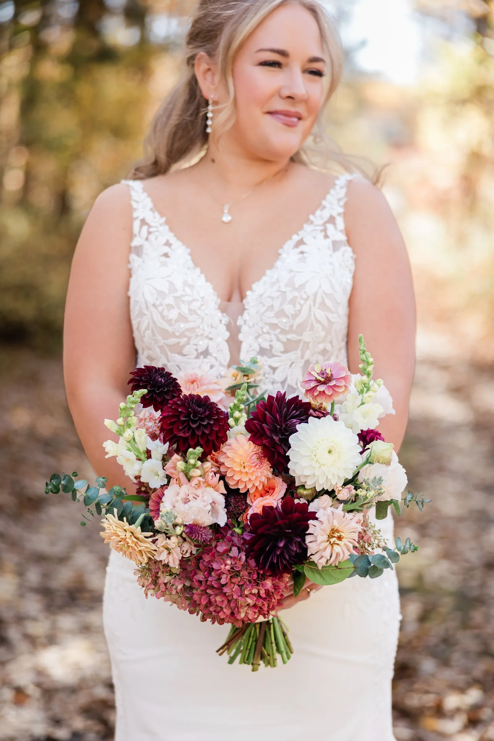 The bride holds a bouquet of deep red, white, and peach flowers with her face softly focused above it — Tim Larsen Photography, Brainerd Lakes MN