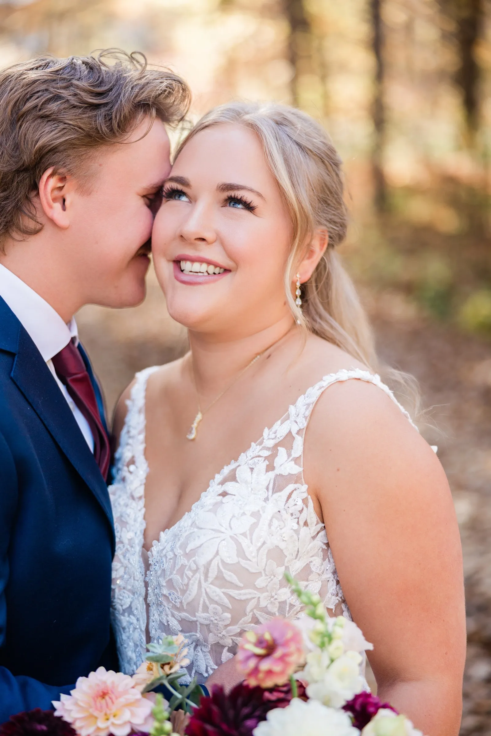 The groom leans his face against the bride's temple while she smiles upward, with flowers at the bottom of the frame — Tim Larsen Photography, Brainerd Lakes MN