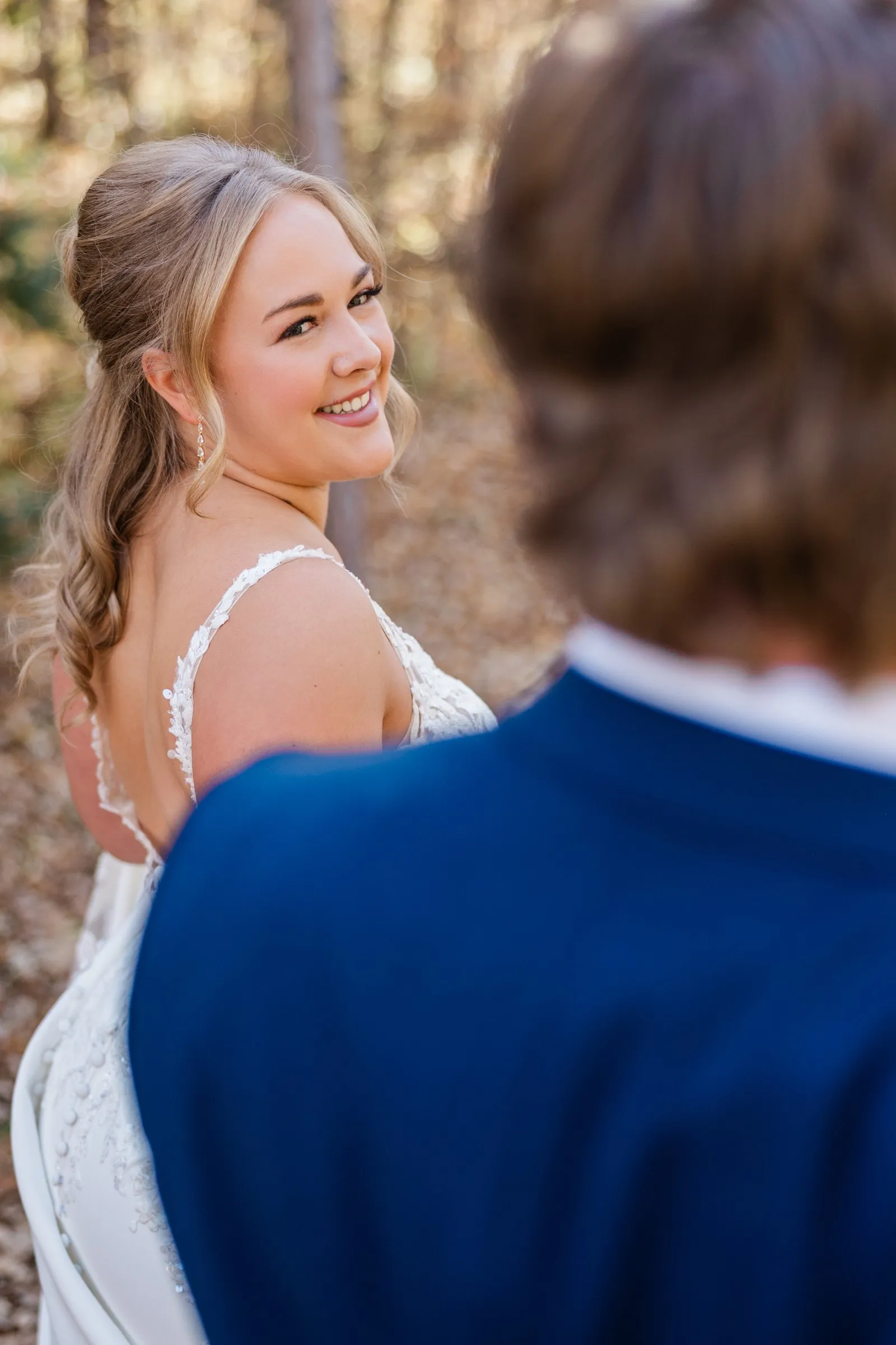The bride smiles back toward the camera with the groom's blue shoulder blurred in the foreground — Tim Larsen Photography, Brainerd Lakes MN