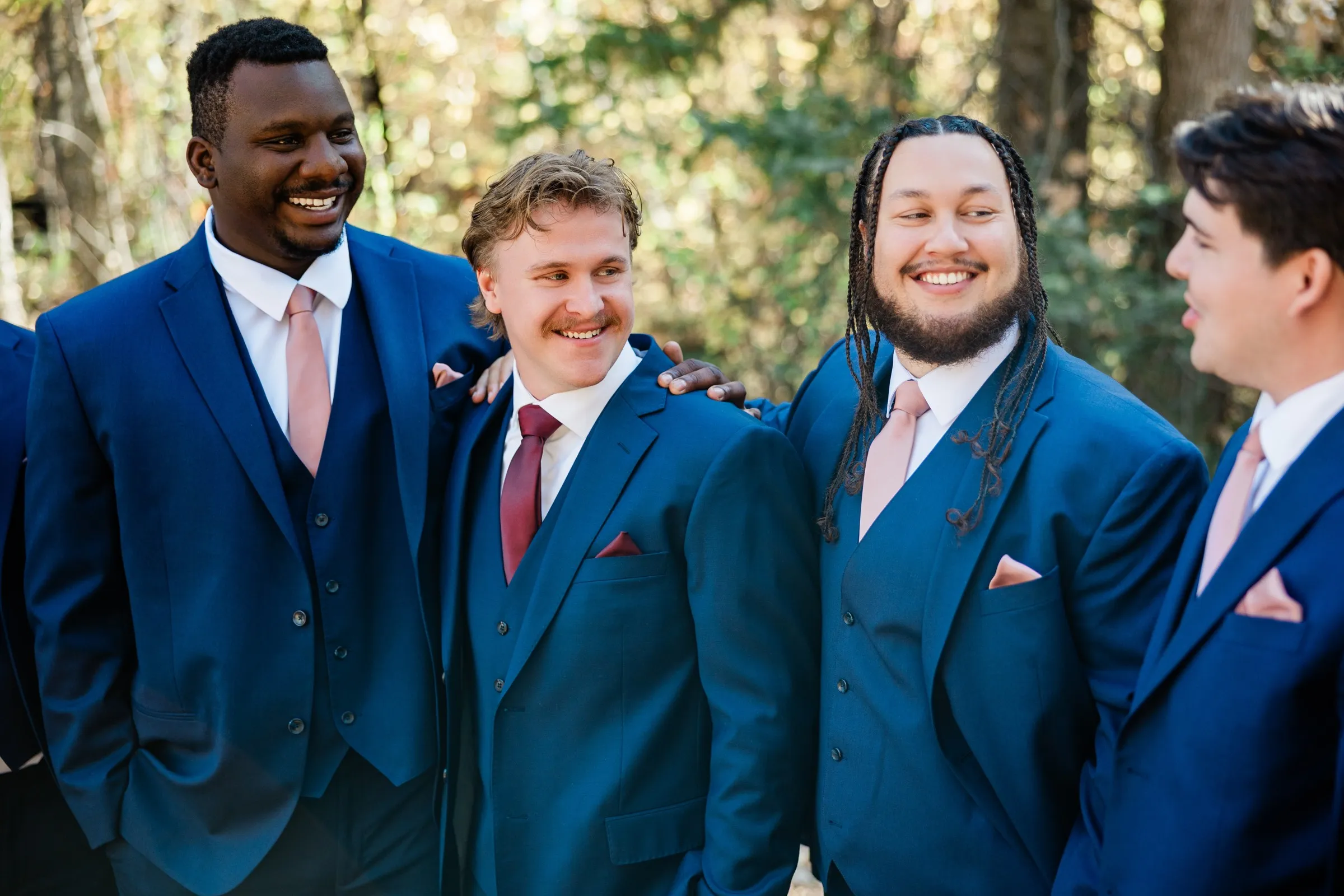 The groom and attendants smile toward one another in a close group portrait, with another figure partly cropped at the left — Tim Larsen Photography, Brainerd Lakes MN