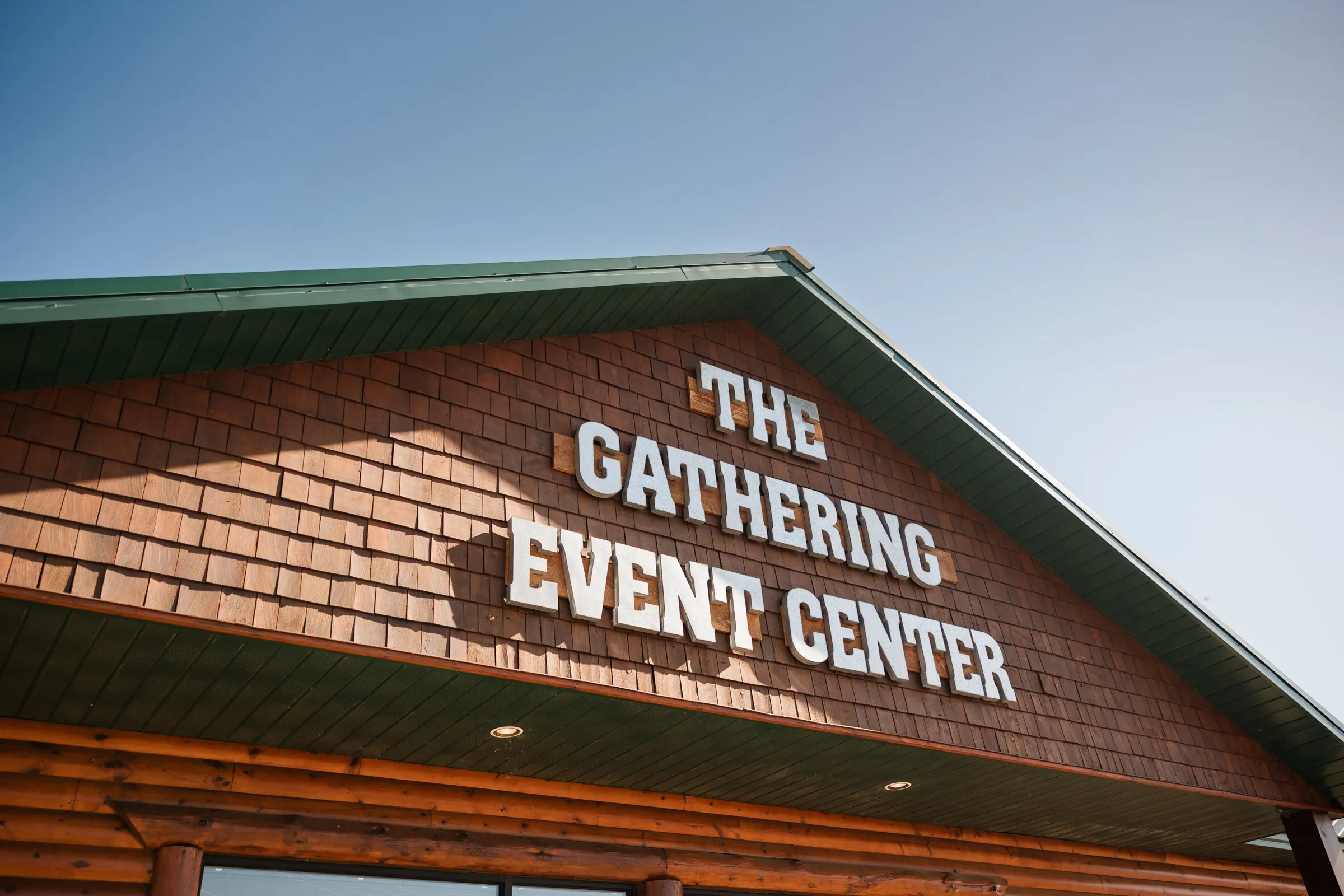 White lettering reading The Gathering Event Center spans the wood-sided entrance beneath a green roof and blue sky — Tim Larsen Photography, Brainerd Lakes MN