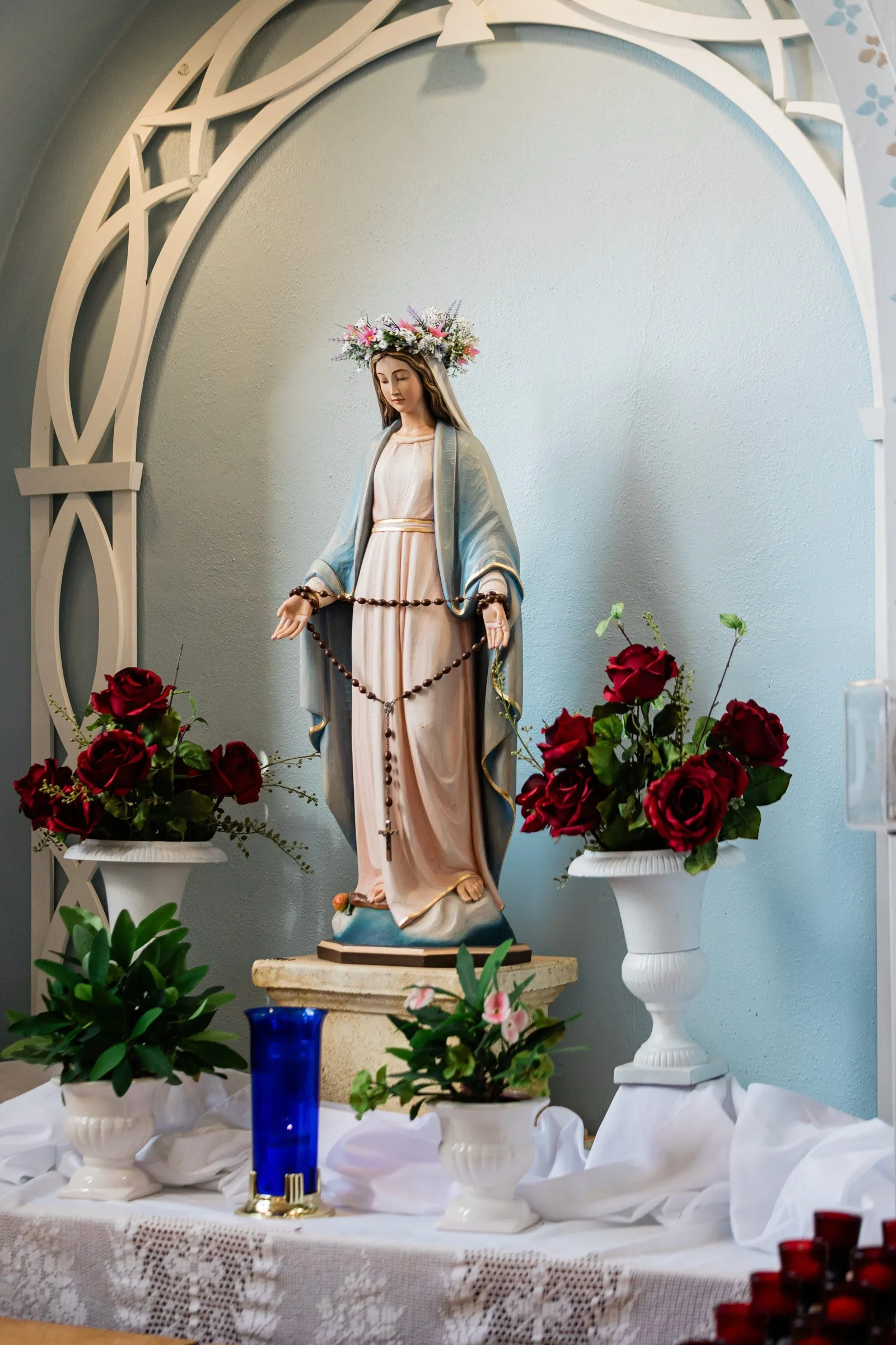 A statue of Mary stands beneath a white arch, surrounded by roses and votive candles at St. Joseph Catholic Church in Crosby — Tim Larsen Photography, Brainerd Lakes MN