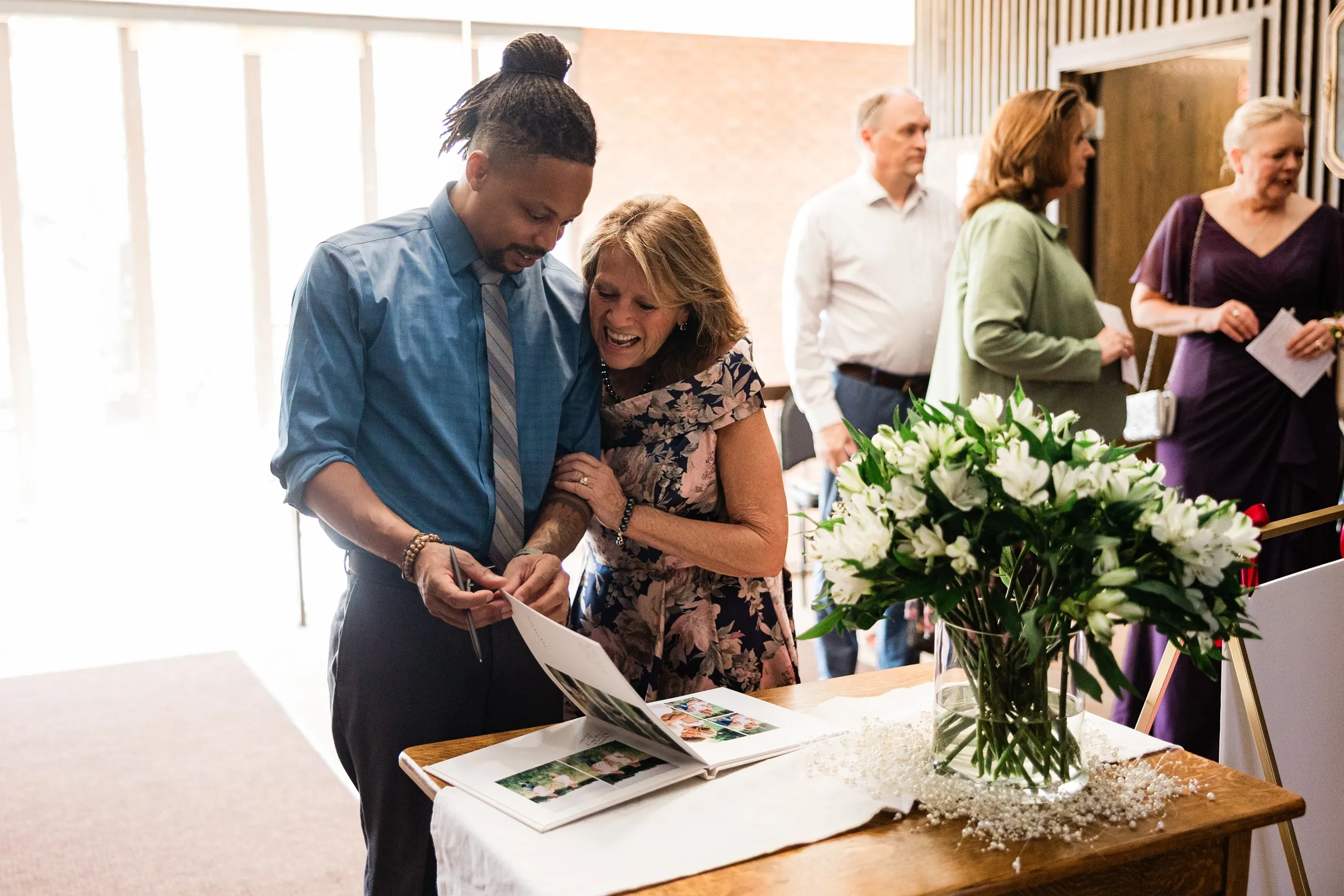 Guests smile over an open photo guest book beside a vase of white flowers in the church entry at St. Joseph Catholic Church in Crosby — Tim Larsen Photography, Brainerd Lakes MN