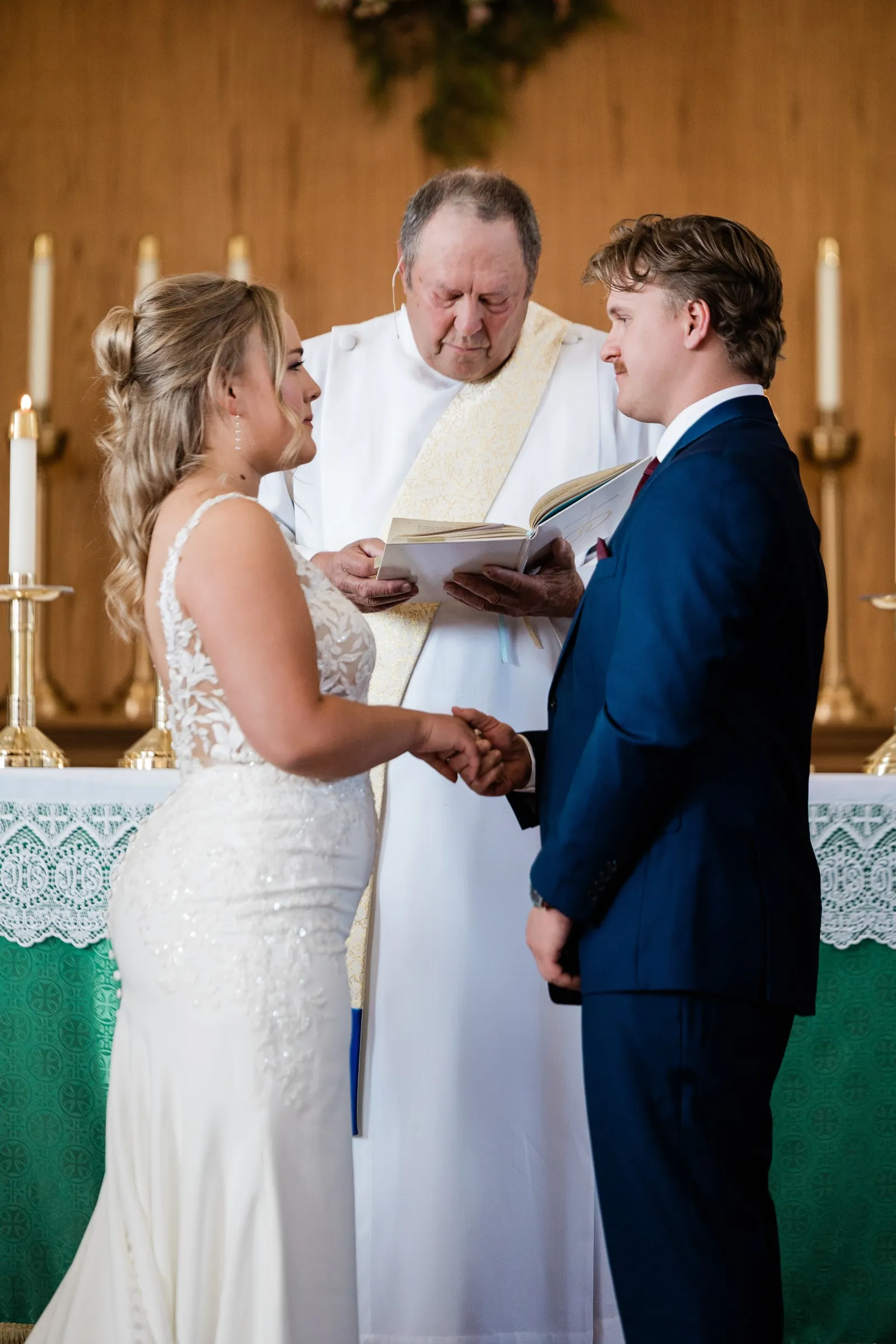 The couple hold hands and look toward each other while the officiant reads in front of the altar at St. Joseph Catholic Church in Crosby — Tim Larsen Photography, Brainerd Lakes MN