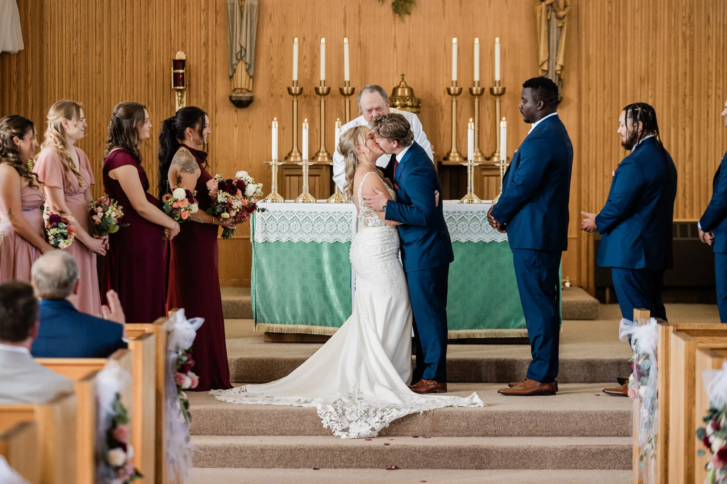 The bride and groom kiss at the altar as their wedding party and seated guests watch at St. Joseph Catholic Church in Crosby — Tim Larsen Photography, Brainerd Lakes MN