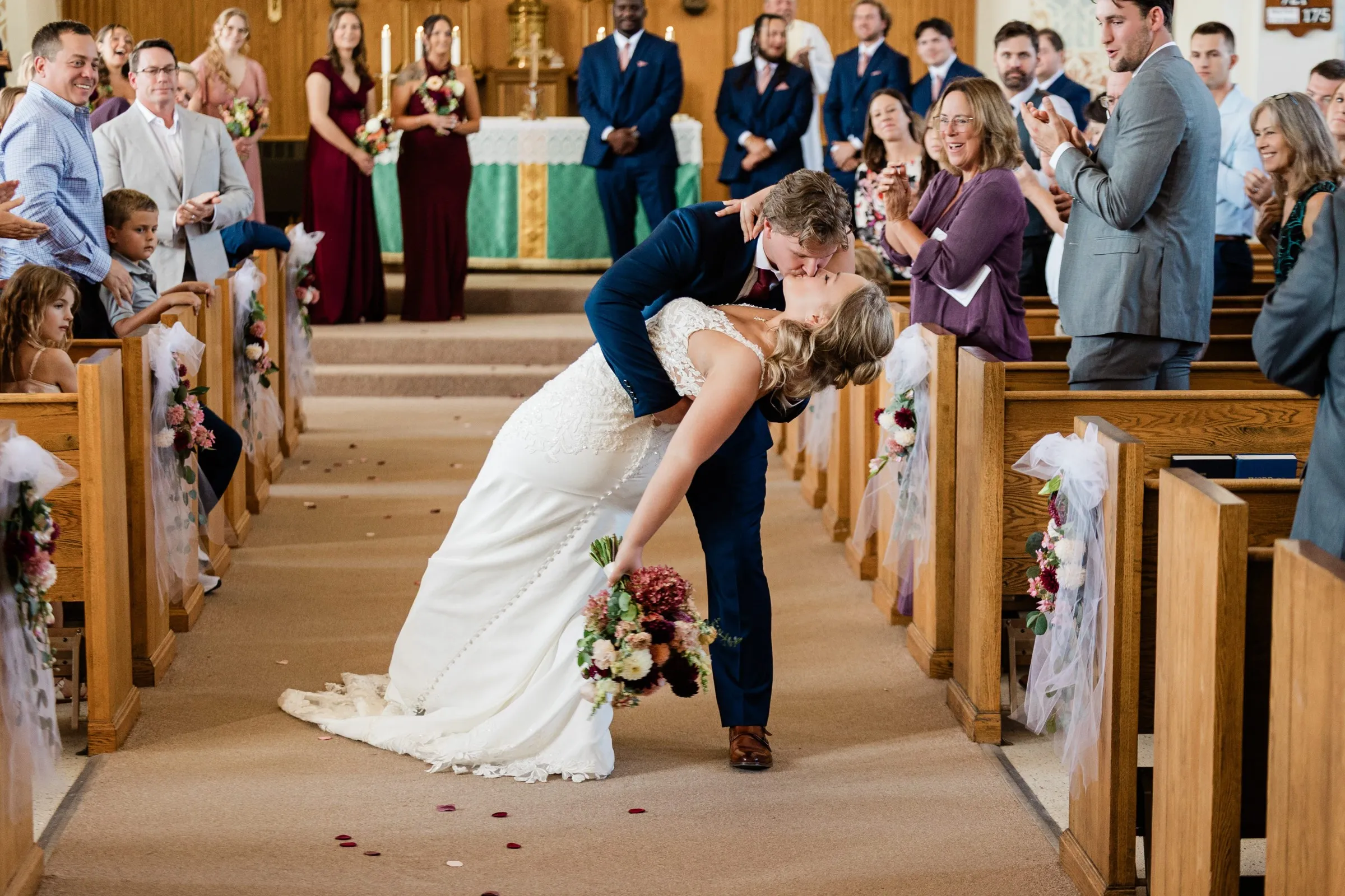 The groom dips the bride for a kiss in the church aisle while guests applaud from both sides at St. Joseph Catholic Church in Crosby — Tim Larsen Photography, Brainerd Lakes MN