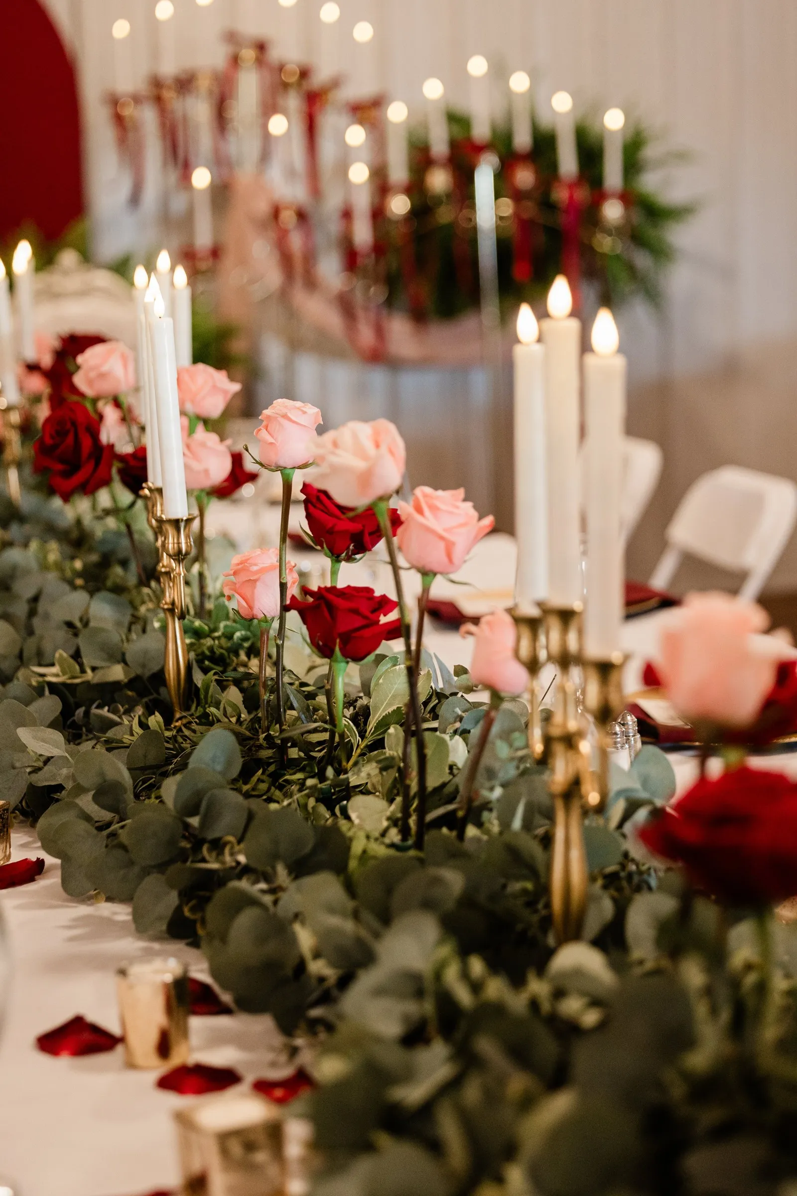 Pink and red roses alternate with gold candleholders along a greenery-covered reception table at The Gathering in Crosslake — Tim Larsen Photography, Brainerd Lakes MN
