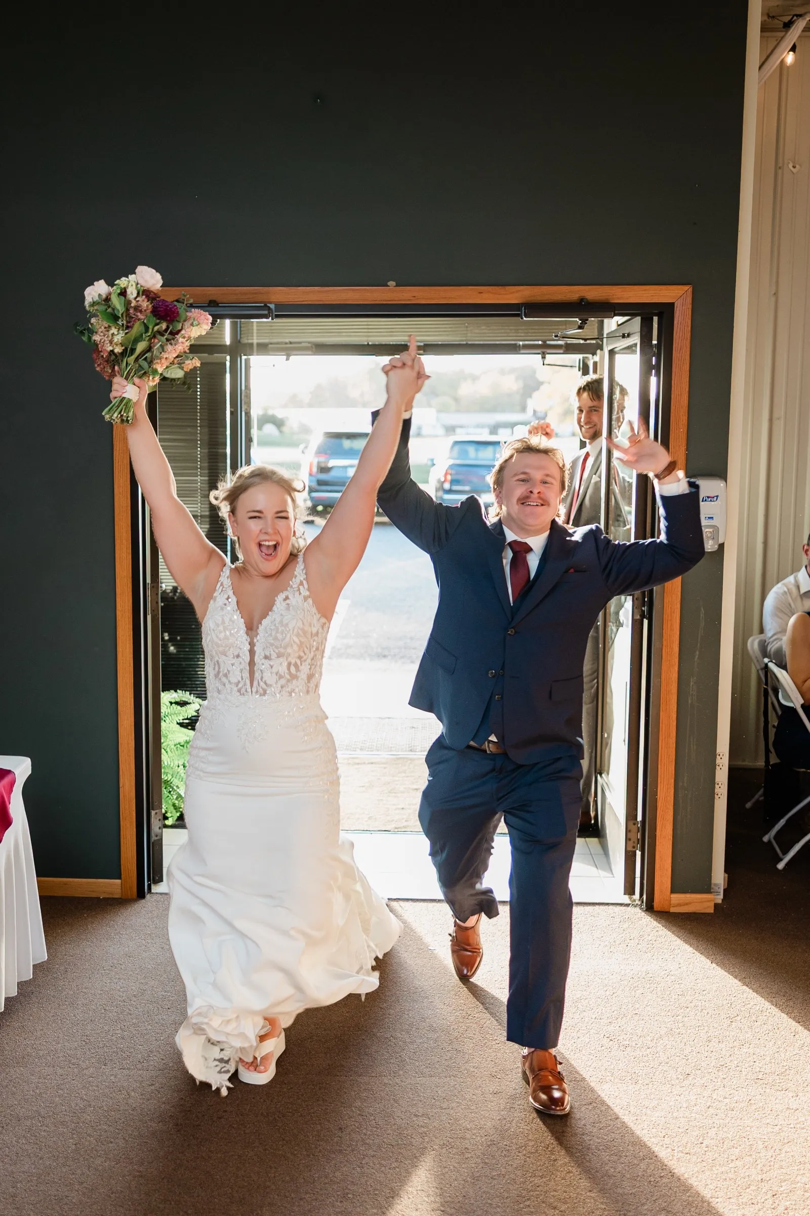 The bride and groom enter the reception with their linked hands raised and the bride’s bouquet held high at The Gathering in Crosslake — Tim Larsen Photography, Brainerd Lakes MN