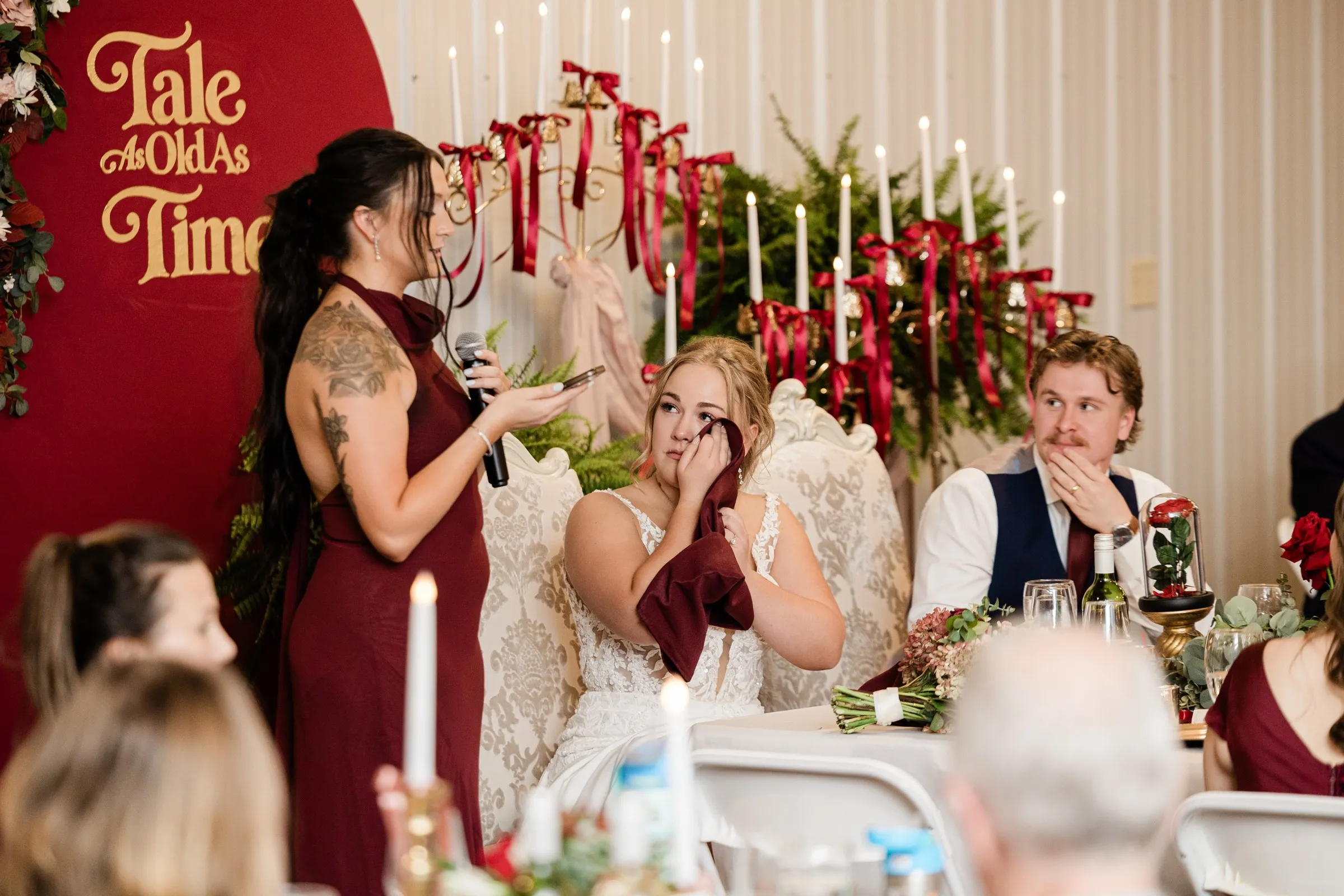 The bride dabs her eye with a burgundy napkin while a bridesmaid speaks beside her and the groom listens at The Gathering in Crosslake — Tim Larsen Photography, Brainerd Lakes MN