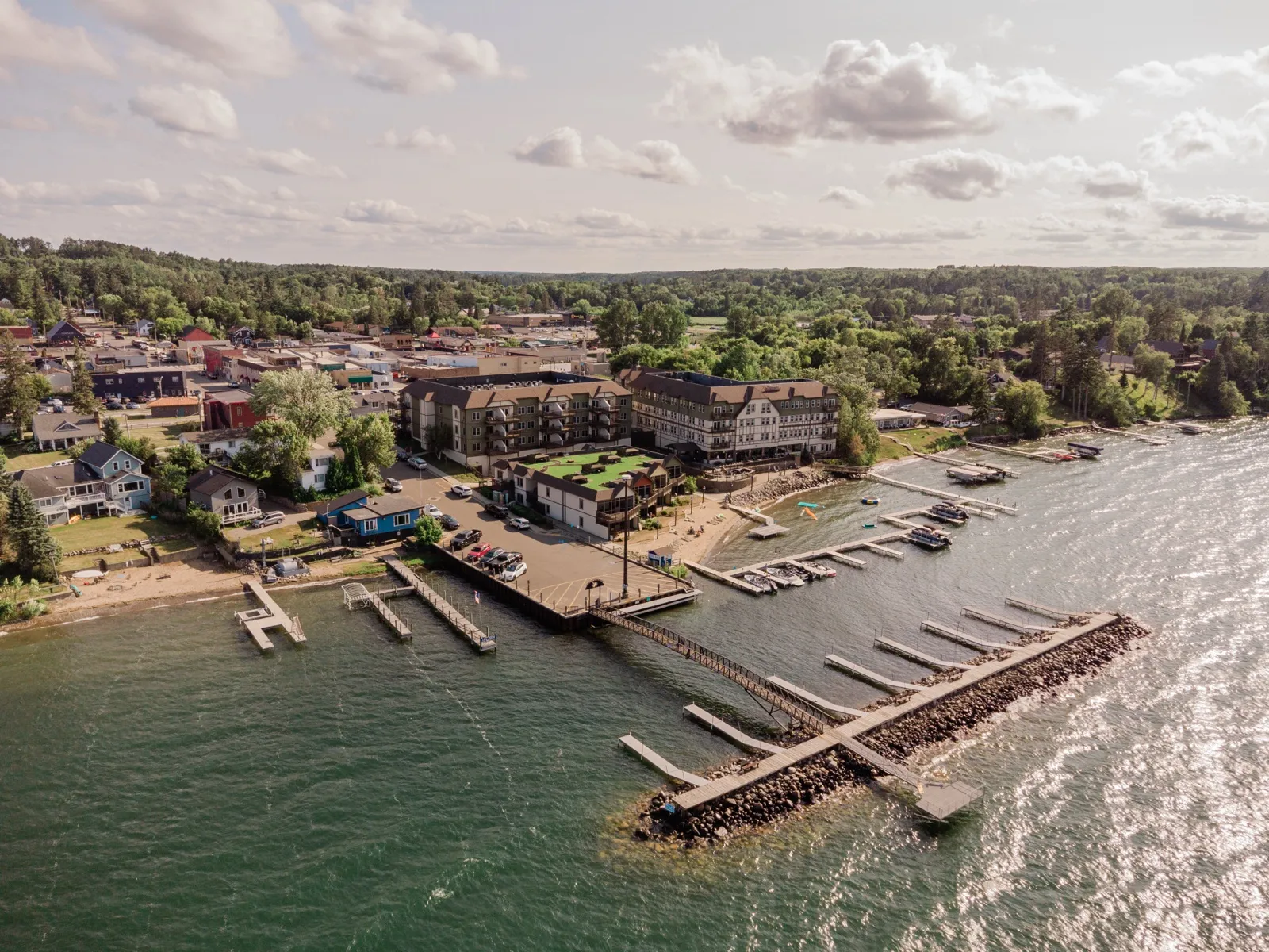 Aerial view of the Chase on the Lake resort and the town of Walker, Minnesota, with a long marina breakwater and boat docks extending into Leech Lake under afternoon sun — Tim Larsen Photography, Brainerd Lakes MN