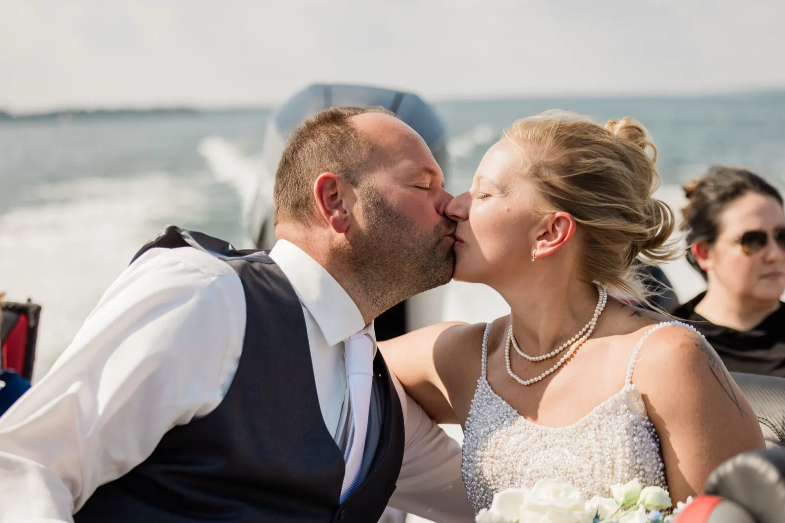 The groom kisses the bride's cheek aboard a moving boat on Leech Lake, the wake trailing behind them — Tim Larsen Photography, Brainerd Lakes MN